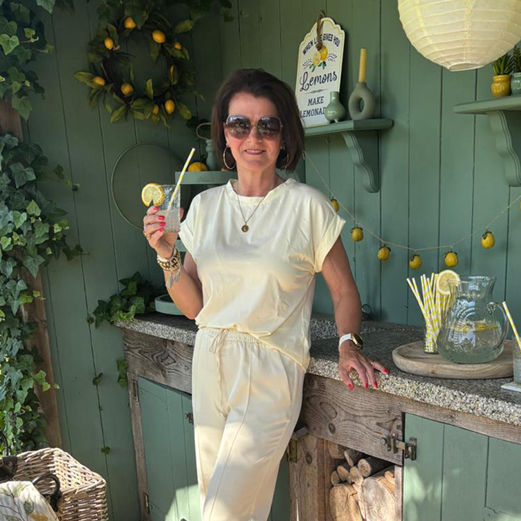 Žena v krémovém oblečení relaxuje s limonádou před zelenou zdí s citronovou výzdobou