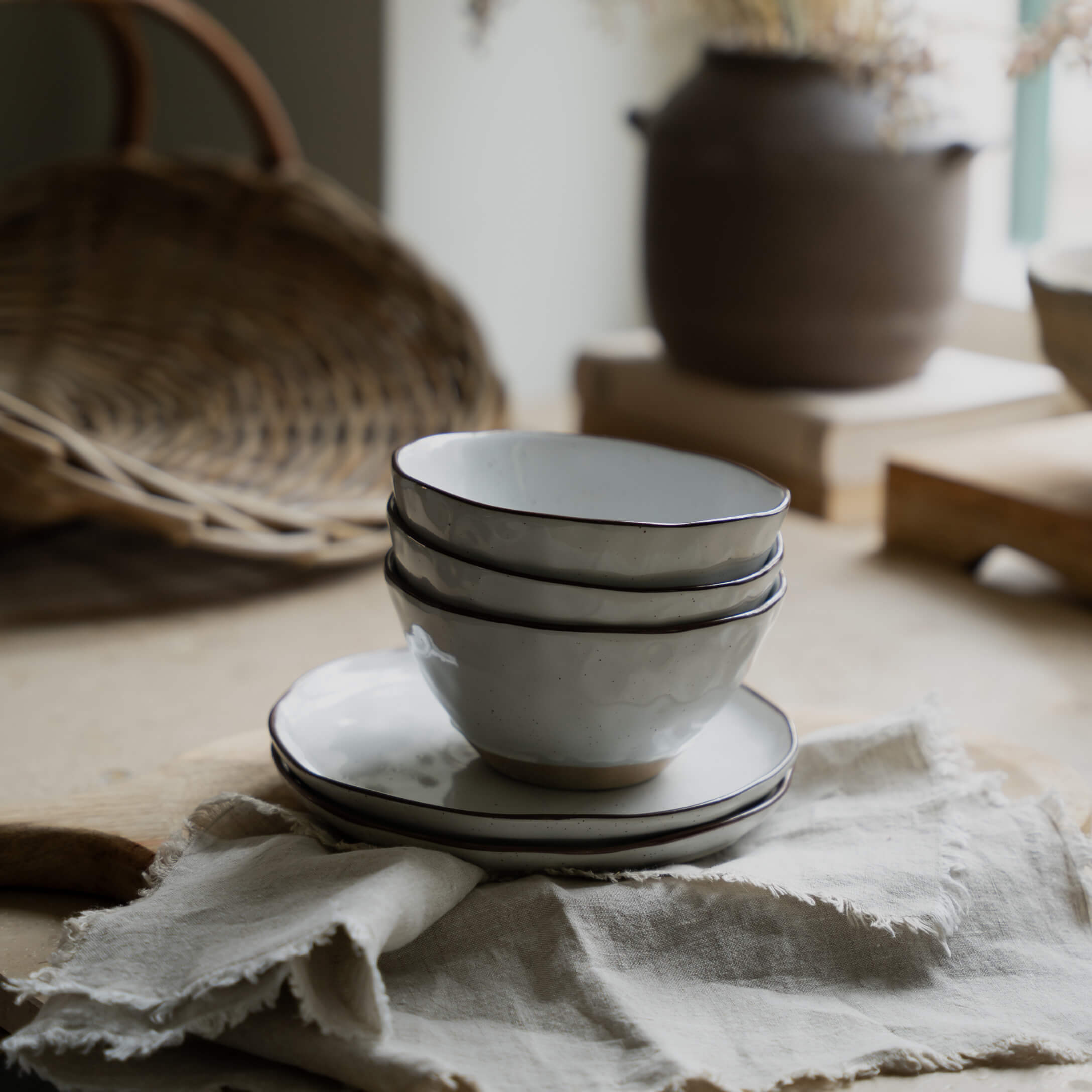 Sada bílých keramických misek a talířů s černým okrajem na lněné látce do kuchyně