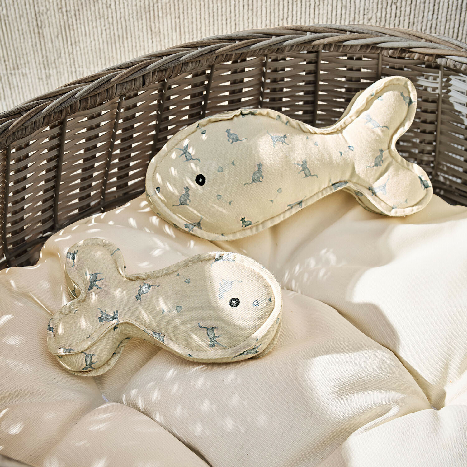 Béžové polštáře ve tvaru ryb s potiskem koček na proutěném křesle s světlým polstrováním