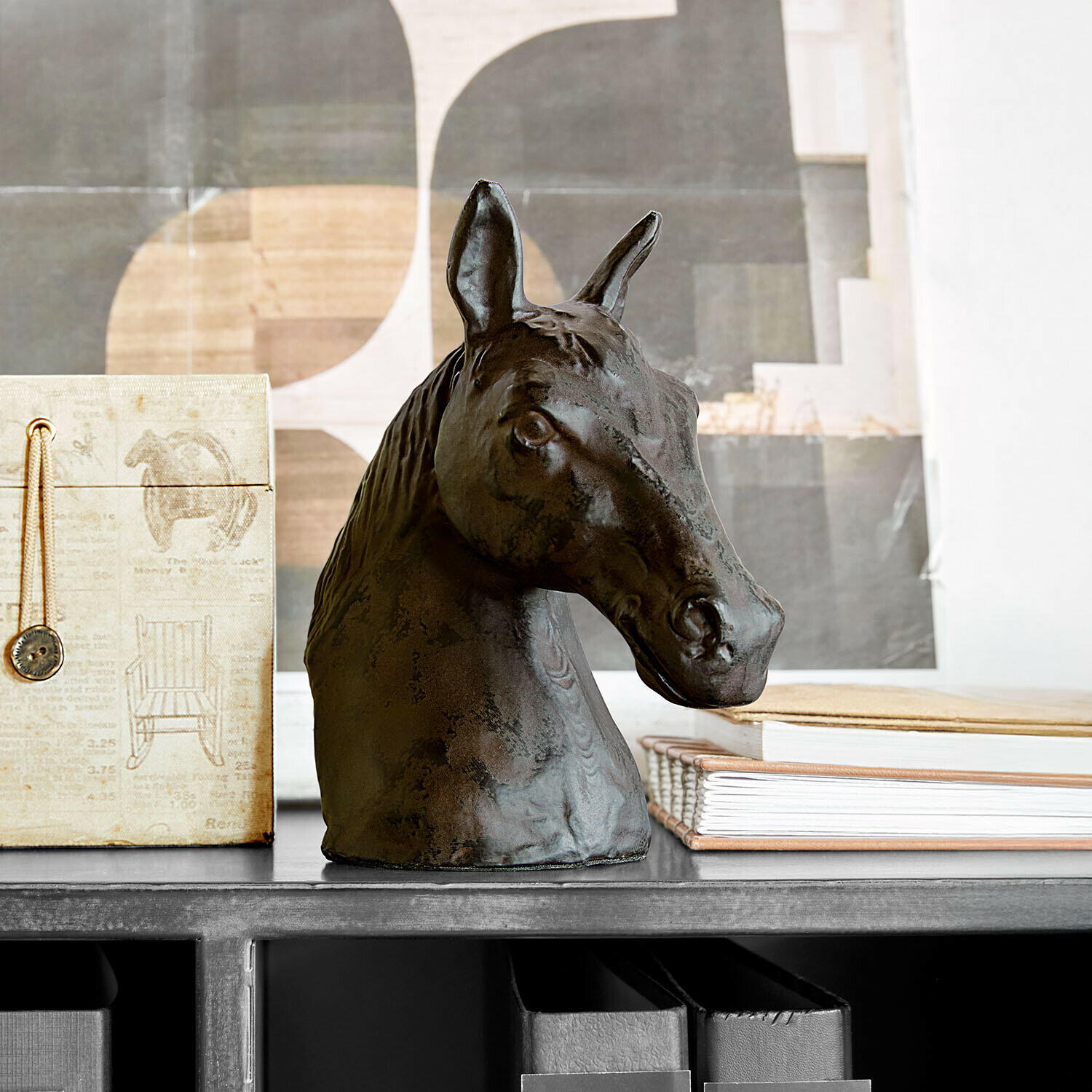 Dekorativní hlava koně z tmavého kovu na polici s knihami a krabicí