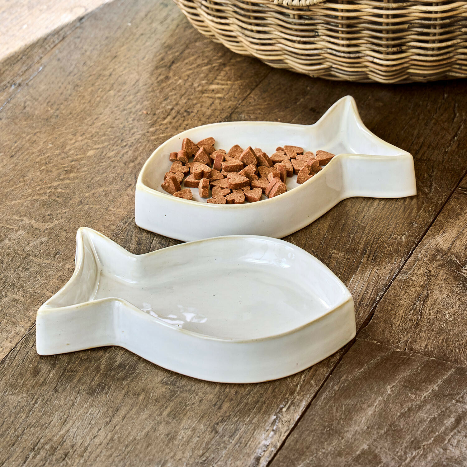 Bílé keramické misky ve tvaru ryby na krmivo pro zvířata na dřevěném stole