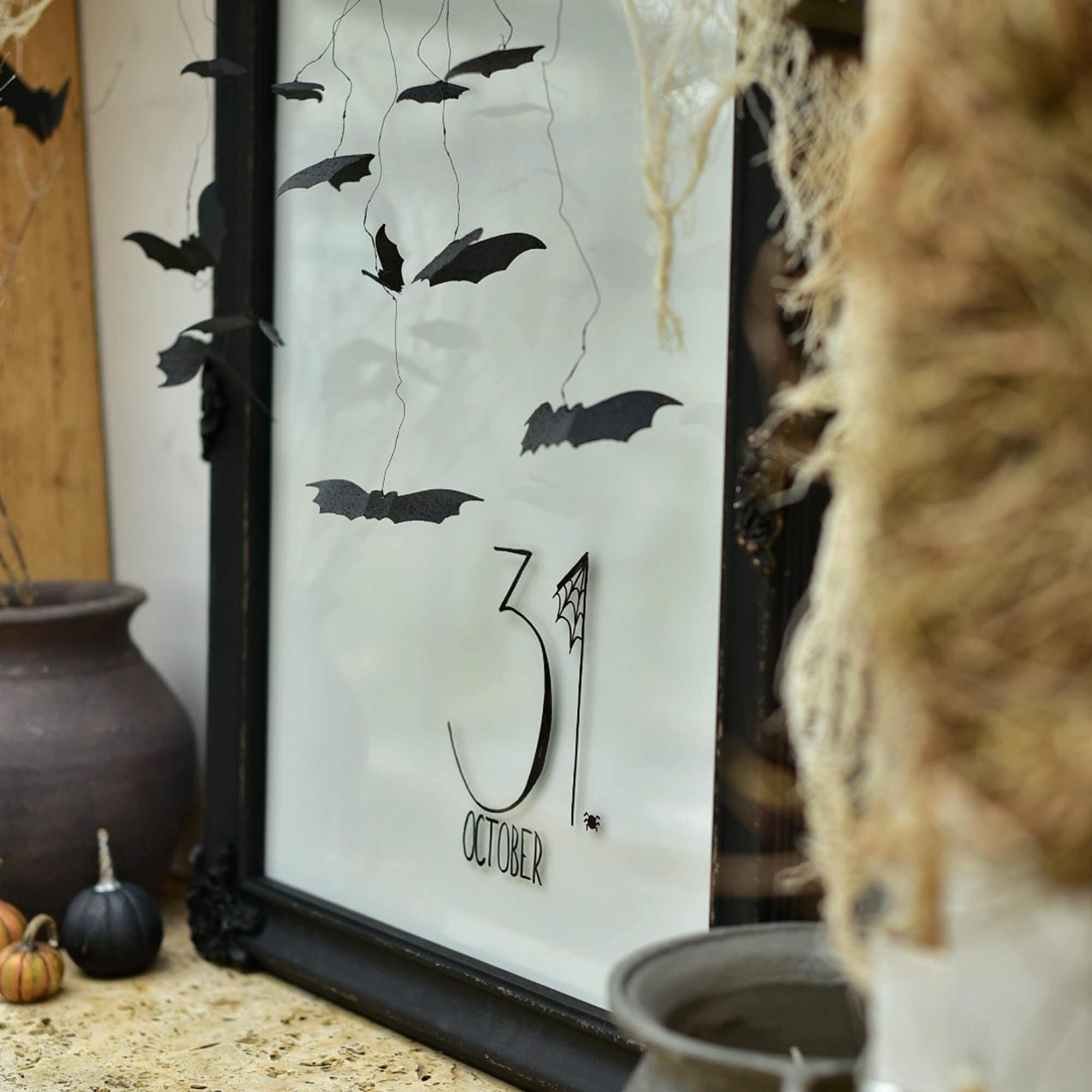 Halloween dekorace s černými papírovými netopýry a nápisem 31. října v rámu