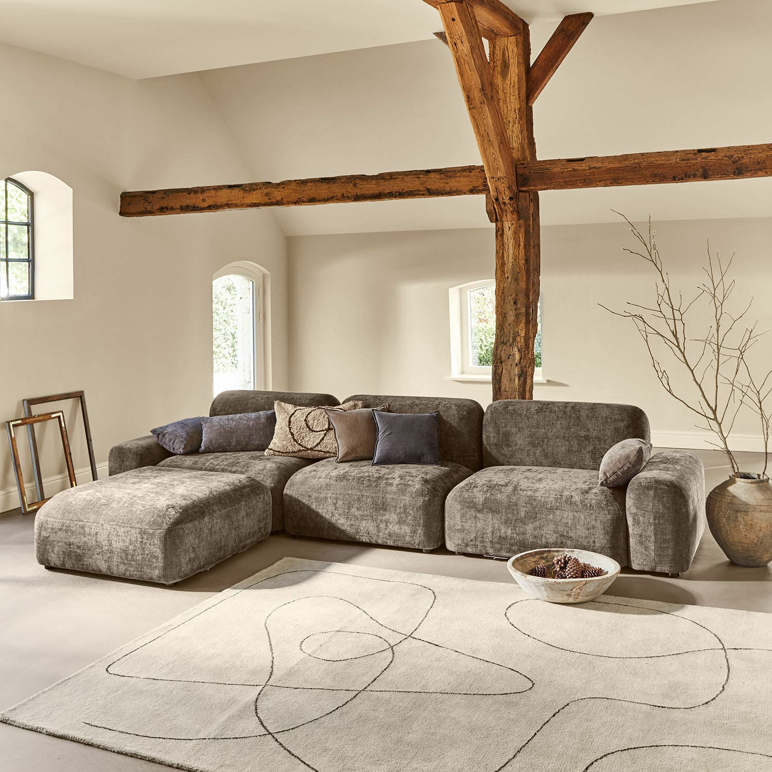 Šedá modulární látková pohovka v moderním obývacím pokoji s dřevěnými trámy a světlým kobercem