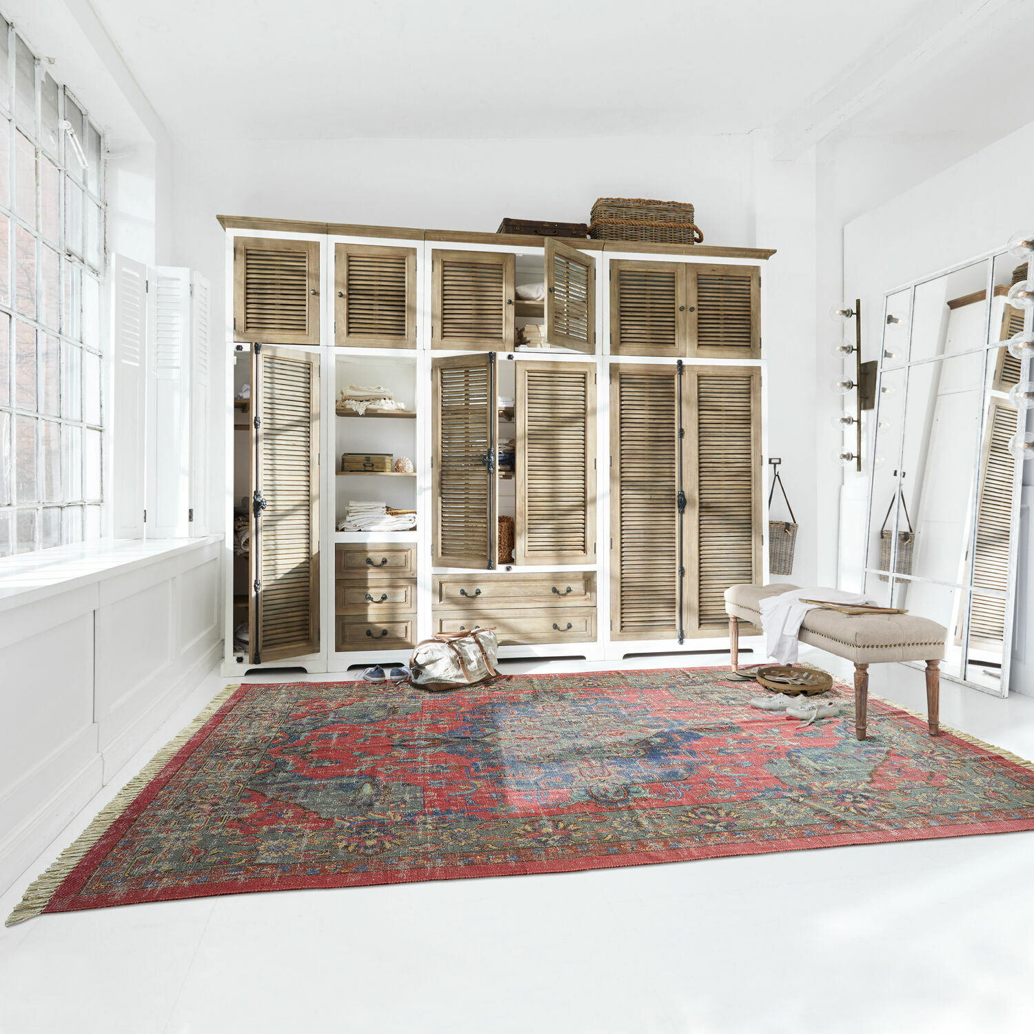 Velký červený koberec s orientálním vzorem v světlé místnosti s dřevěnou skříní a lavicí