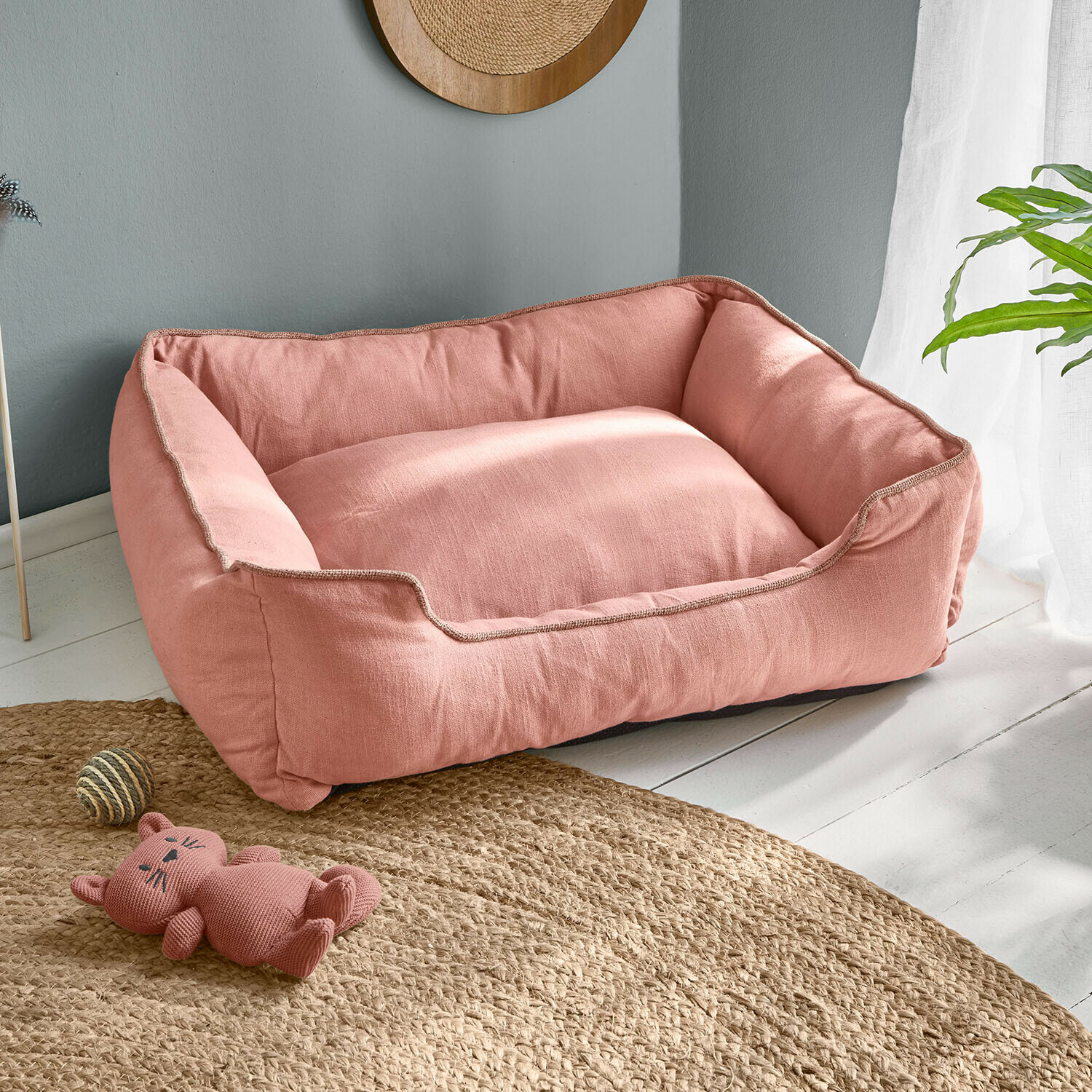 Růžový pelíšek pro psa z měkkého materiálu na světlé podlaze s hračkou kočky a míčkem