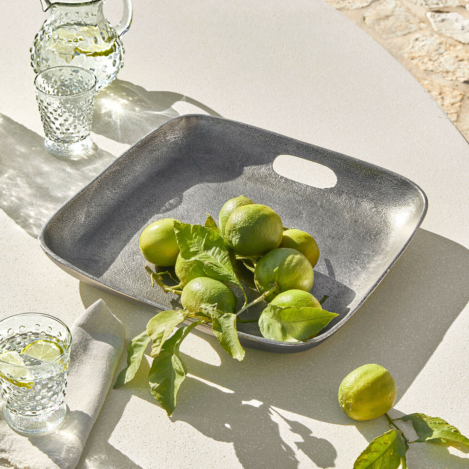 Čtvercový šedý kovový tác s limetkami na světlém stole, letní stolní dekorace