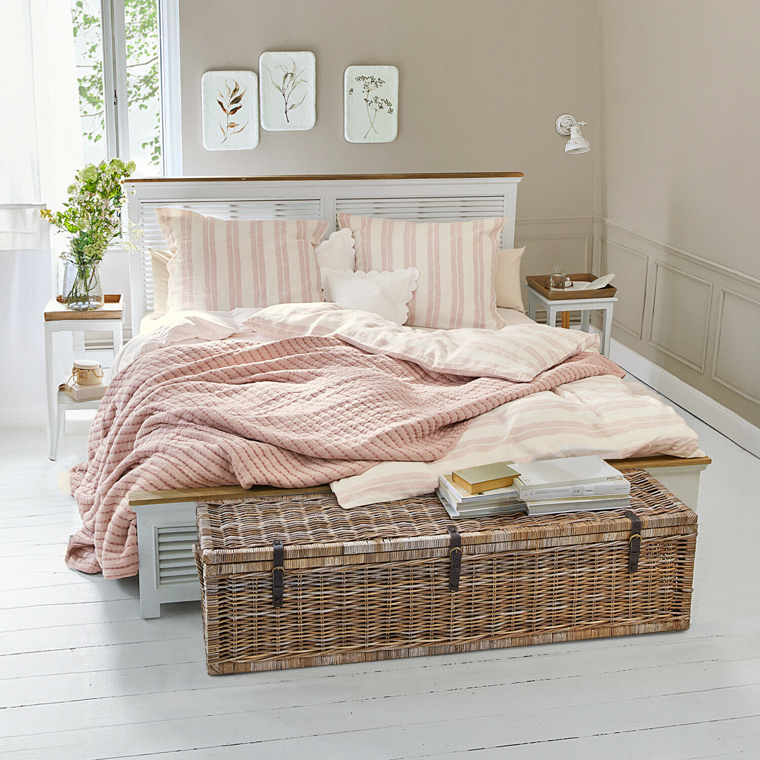 Pohodlná ložnice s postelí v světle růžových pruzích a proutěnou truhlicí na bílých podlahách