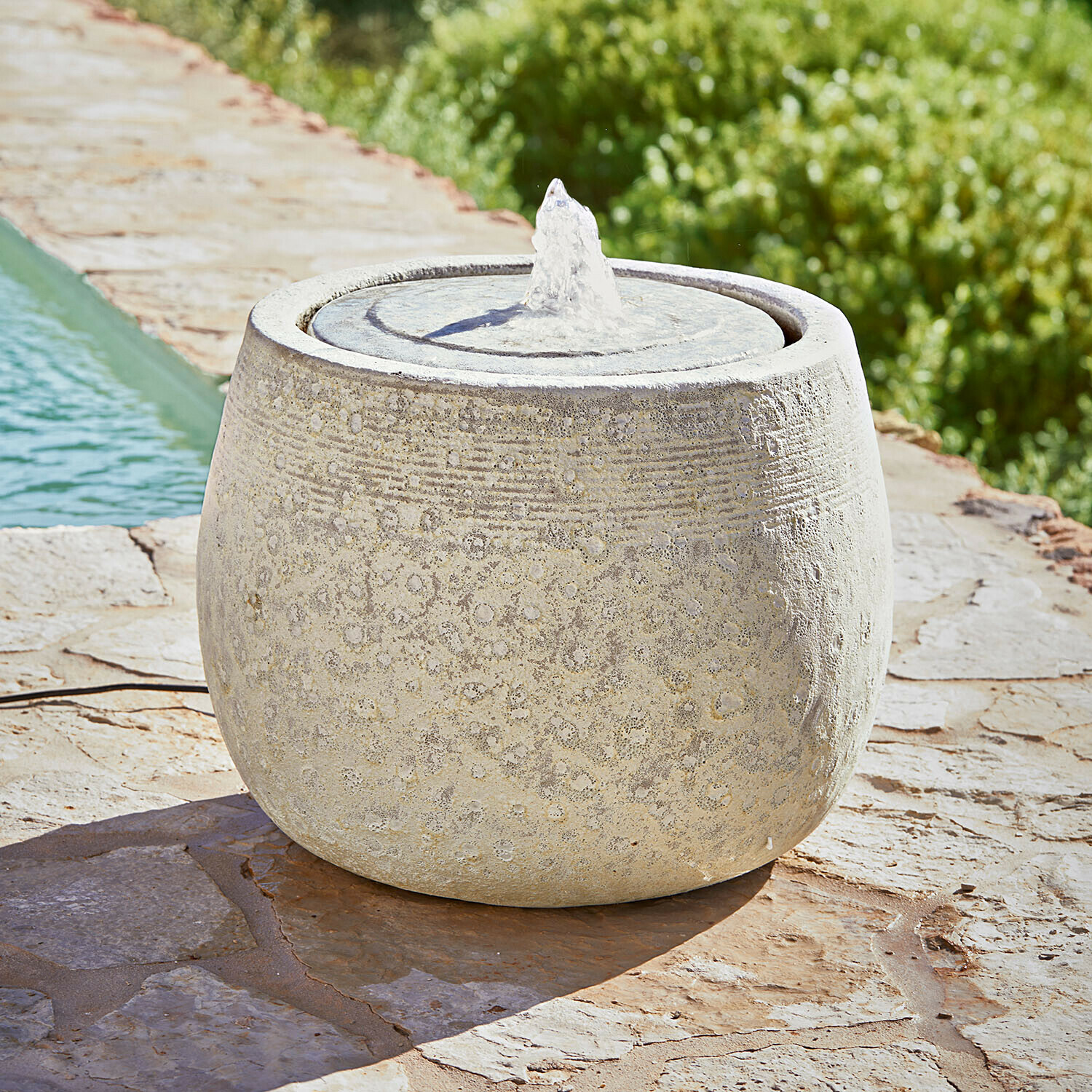 Kulatá zahradní fontána z světlého kamene s jemným vzorem a proudem vody na kamenné terase