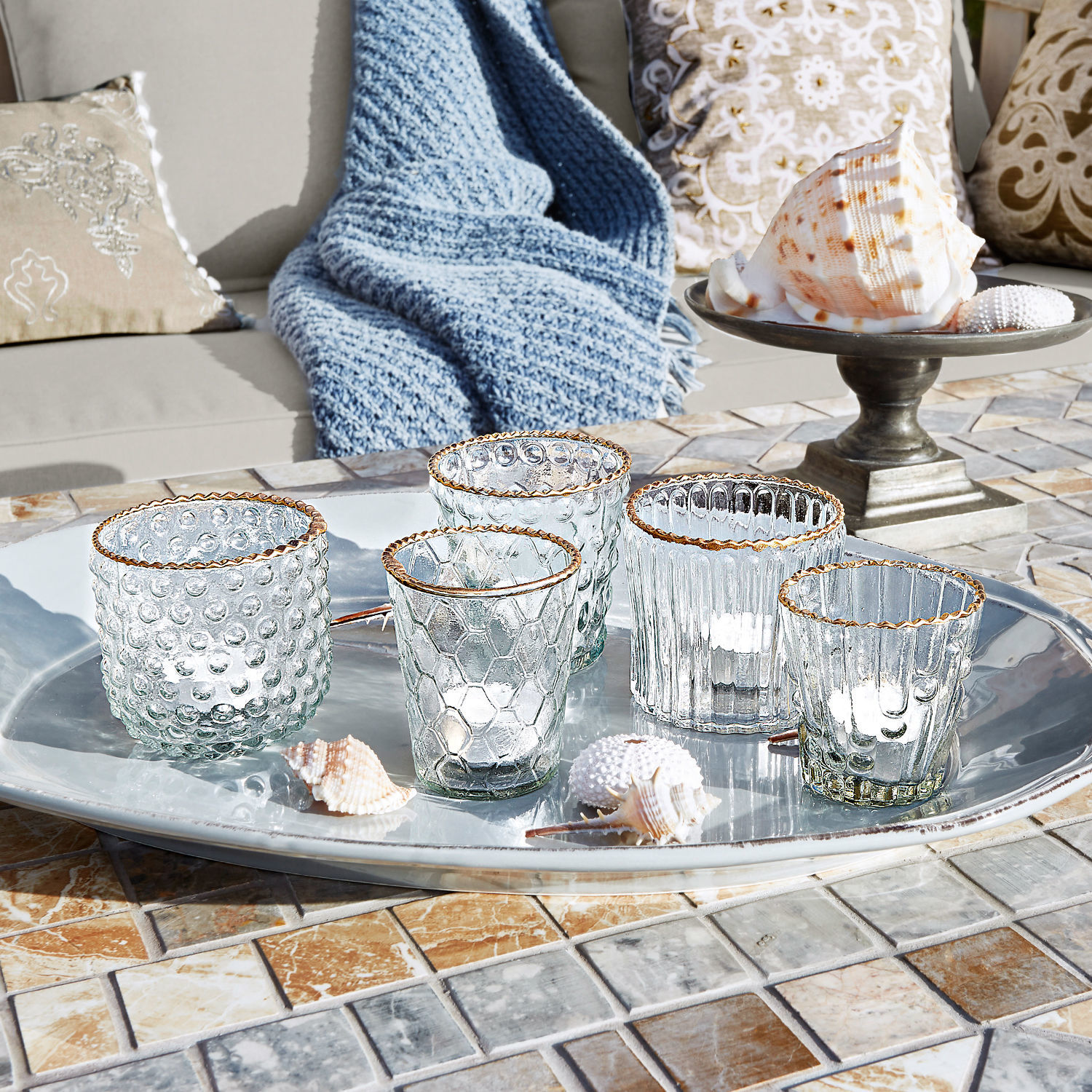 Sada pěti skleněných svícnů se zlatým okrajem na stříbrném podnosu na mozaikovém stole
