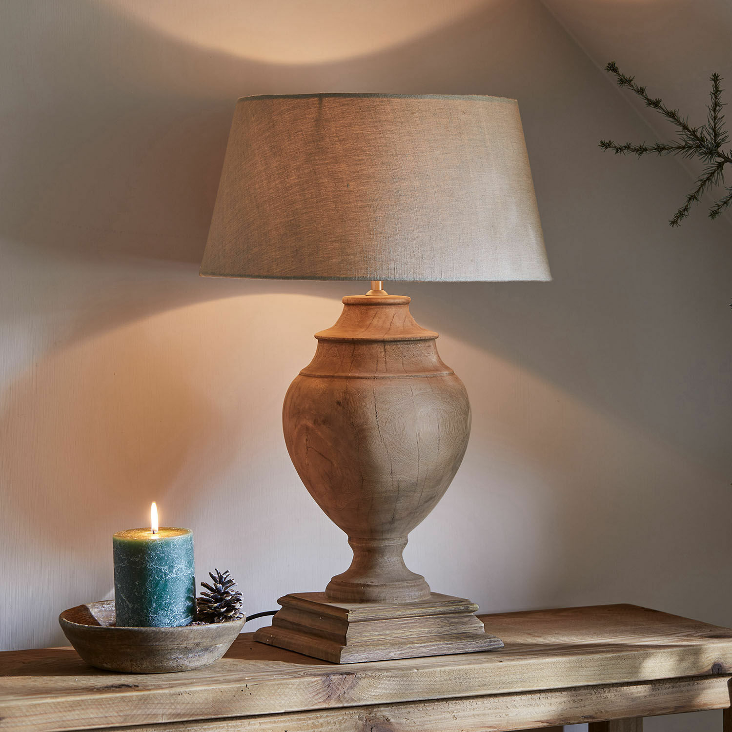 Stolní lampa Sauverny Stolní lampa s dřevěnou základnou a béžovým stínidlem na dřevěném stole, vedle dekorativní svíčka