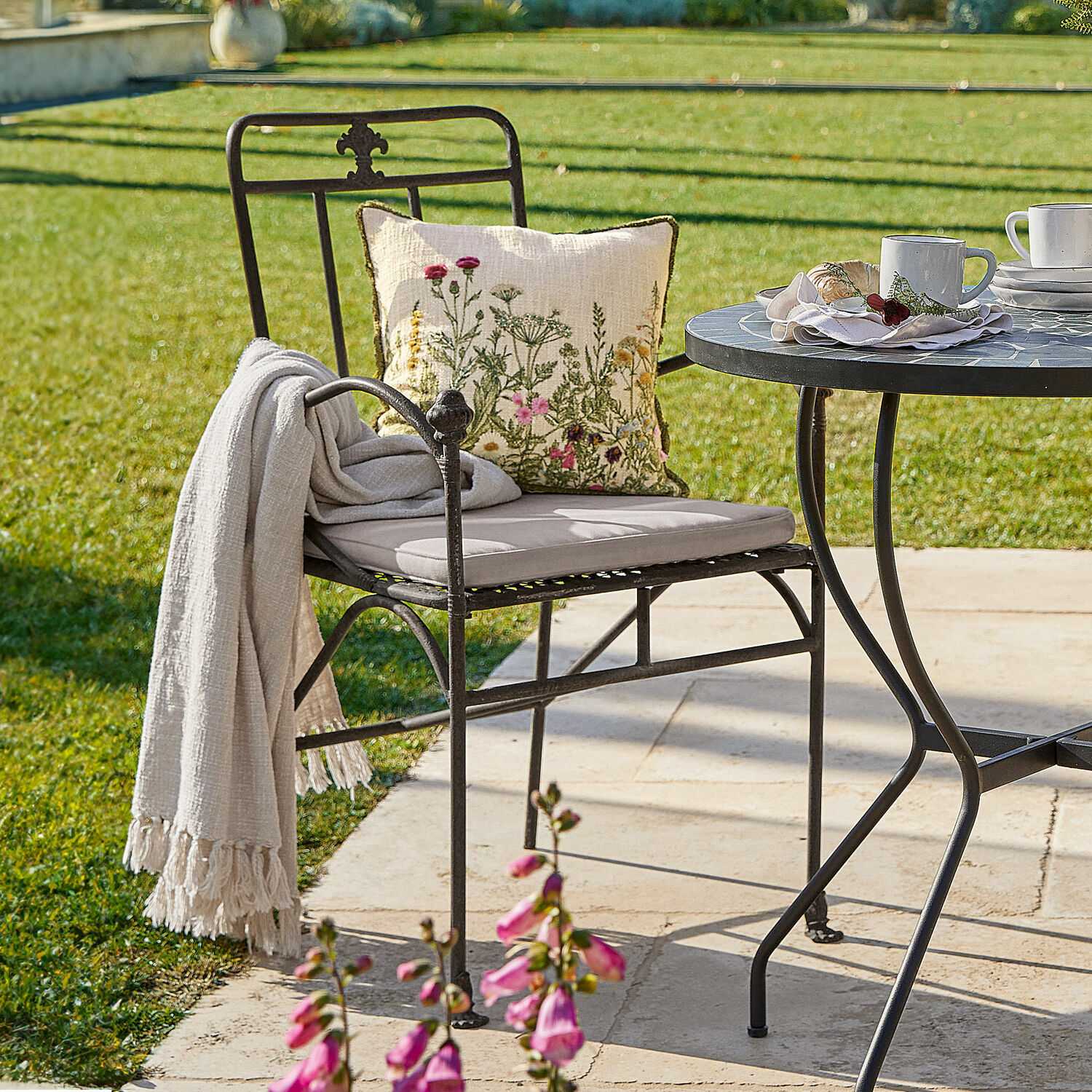 Židle Maidis Černá kovová zahradní židle s světlým polštářem a květinovým dekoračním polštářem na terase