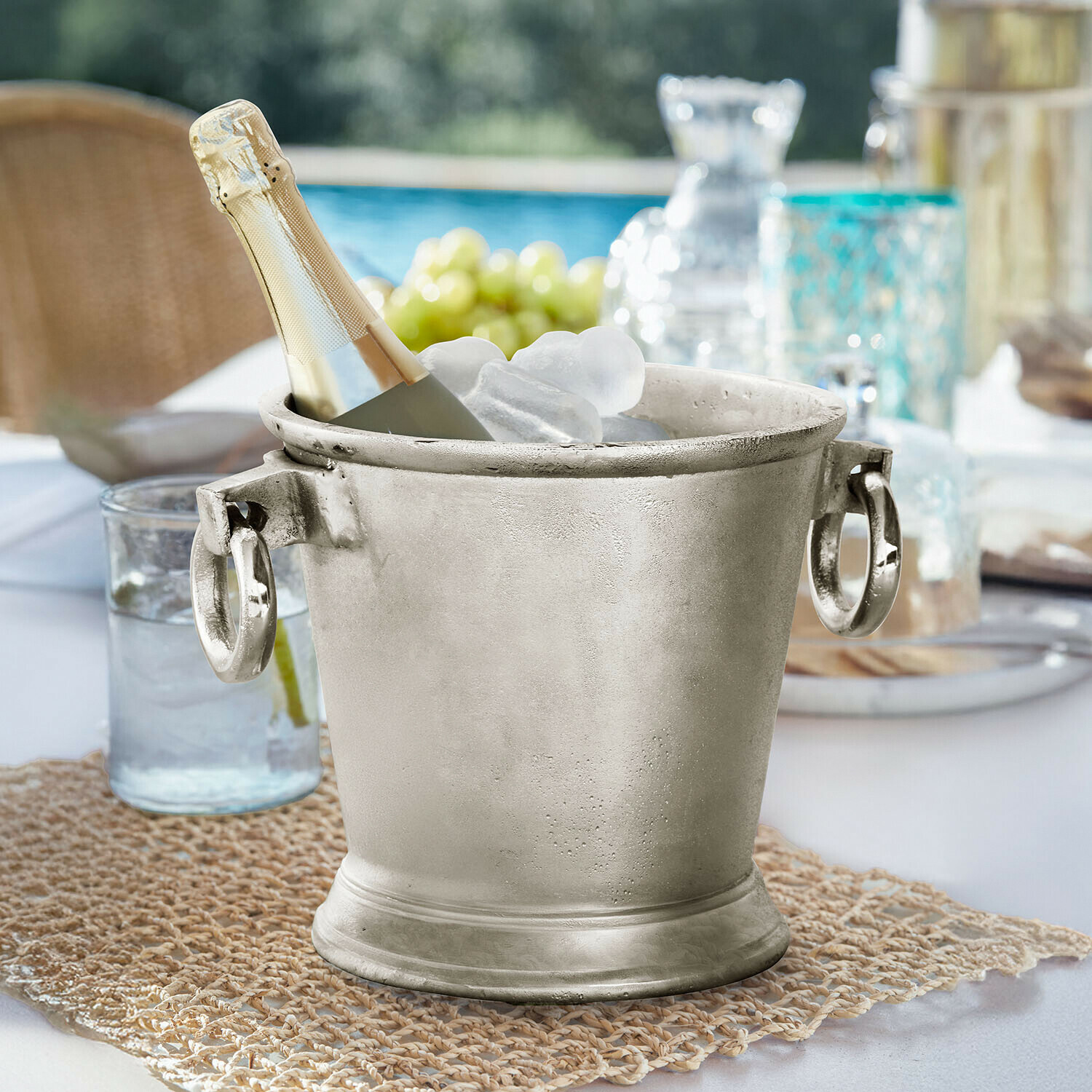 Stříbrný kovový kýbl na led s lahví šampaňského a ledem na zahradním stole