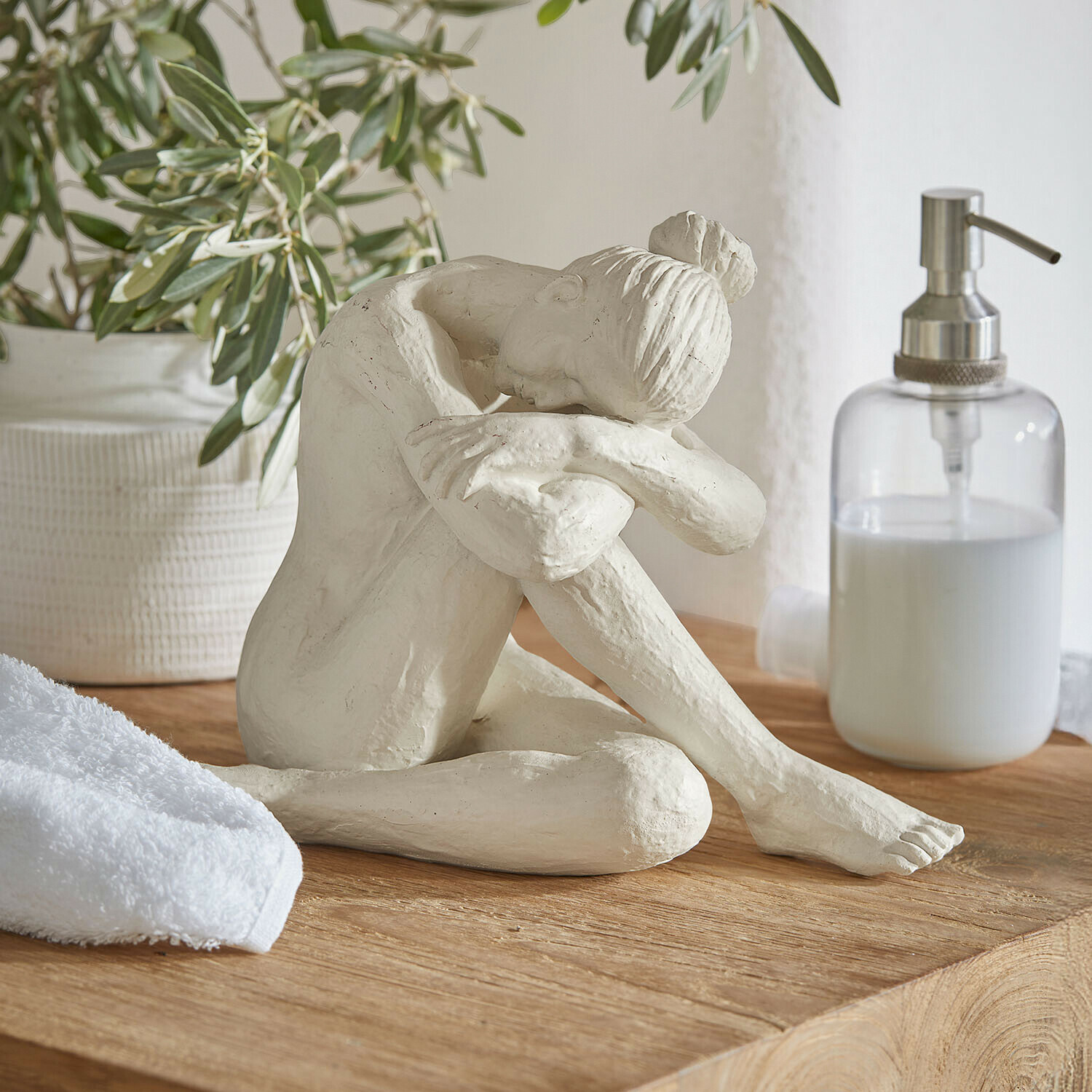 Bílá socha ženy sedící s hlavou na pokrčených kolenou na dřevěném povrchu v koupelně