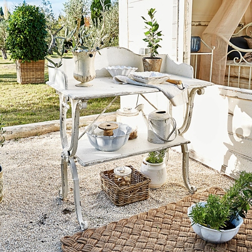 Bílý kovový zahradní stolek ve stylu shabby chic s dekoracemi a rostlinami na terase