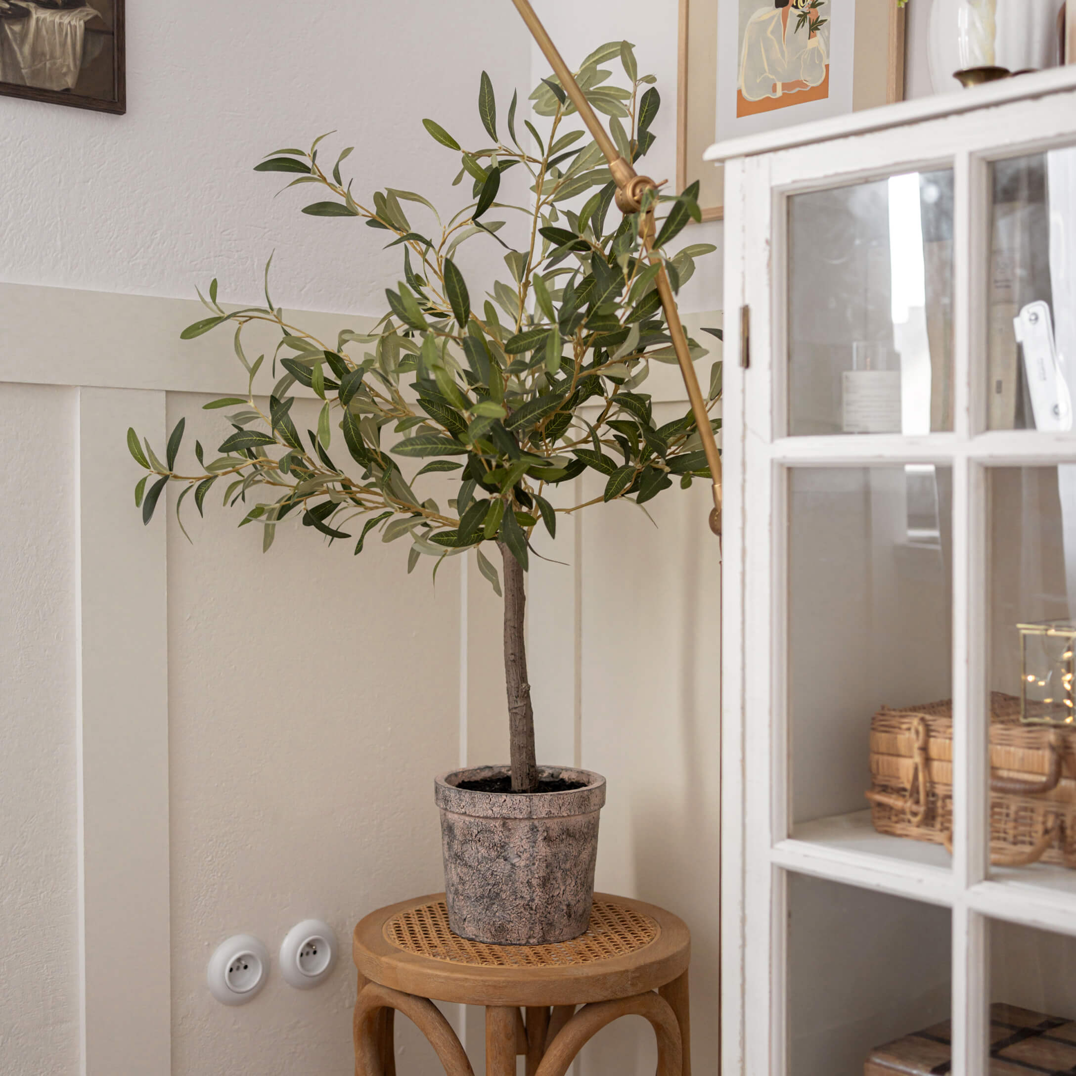 Umělý olivovník v kamenném květináči na dřevěné stoličce v světlém interiéru