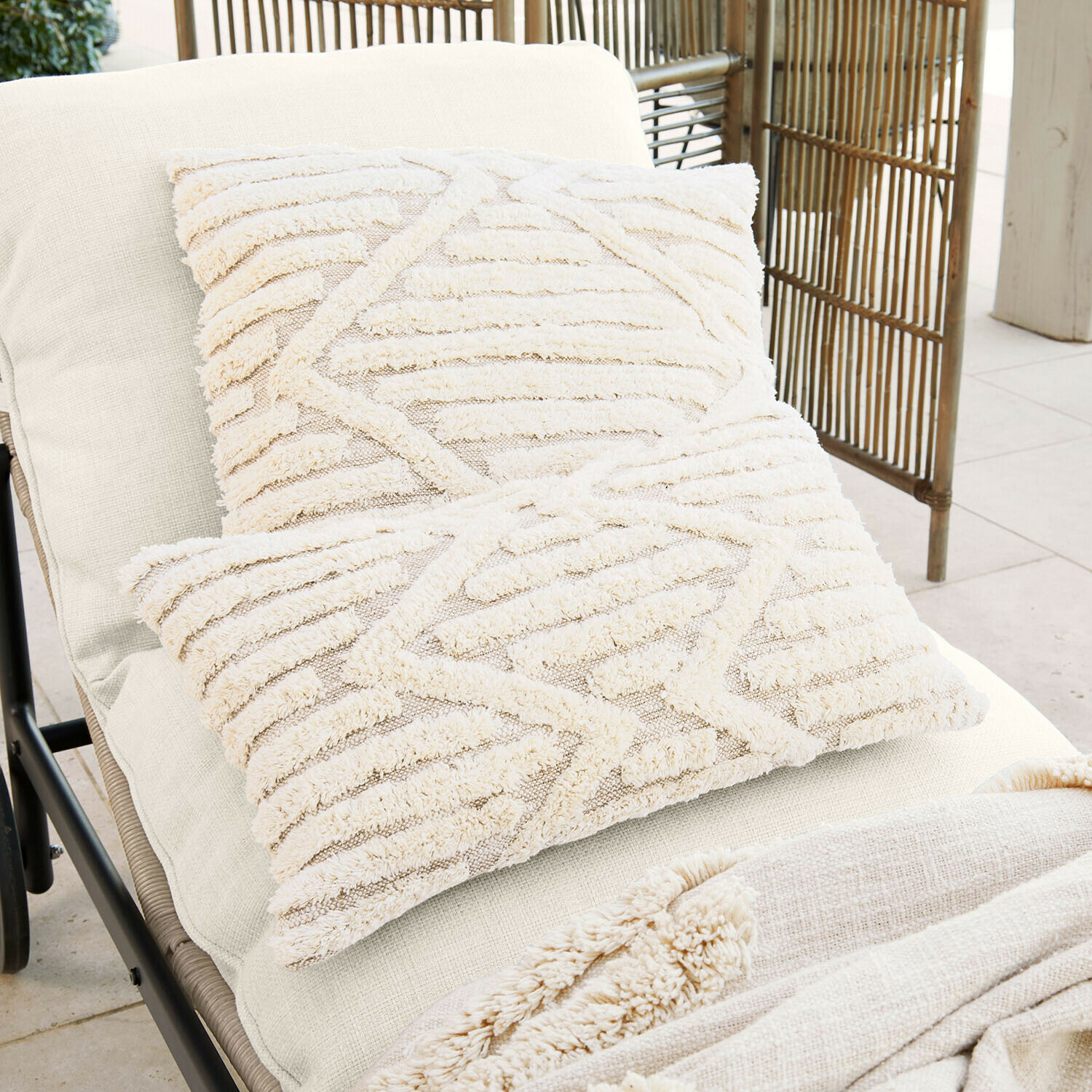 Dva krémové dekorativní polštáře z měkkého materiálu s geometrickým vzorem na světlém lehátku