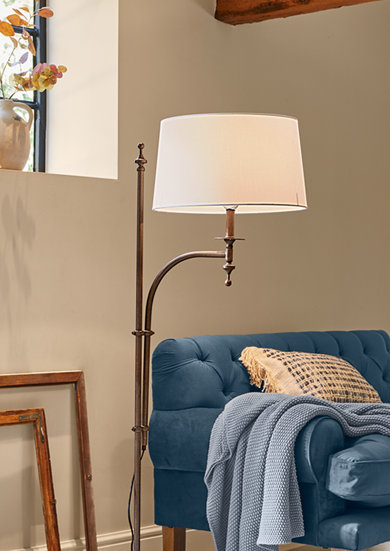 Stojací lampa s kovovým rámem a bílým stínidlem vedle modré pohovky s pletenou dekou