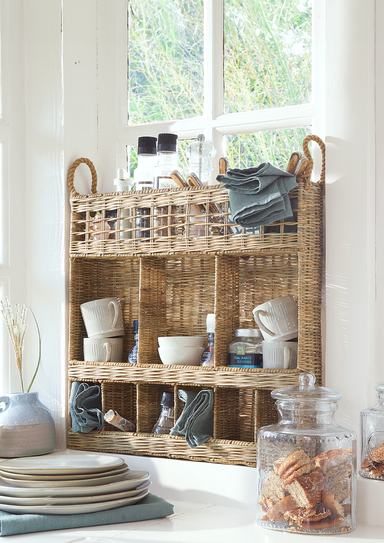 Proutěná kuchyňská police s přihrádkami na koření, hrnky a látkové ubrousky v přírodní barvě