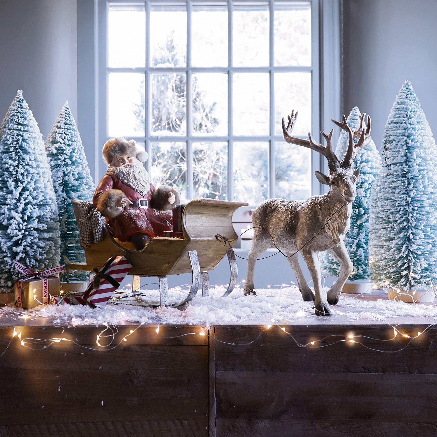 Vánoční sáňky Palaima Figurka Santa Clause v červeném plášti na dřevěných saních s jelenem a zasněženými stromy