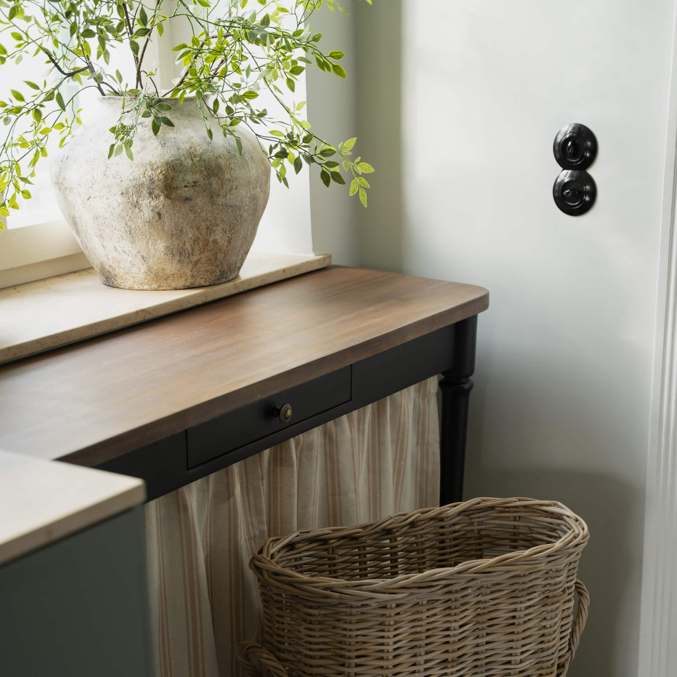 Rustikální světlá kamenná váza se zelenými větvičkami na tmavém dřevěném stole