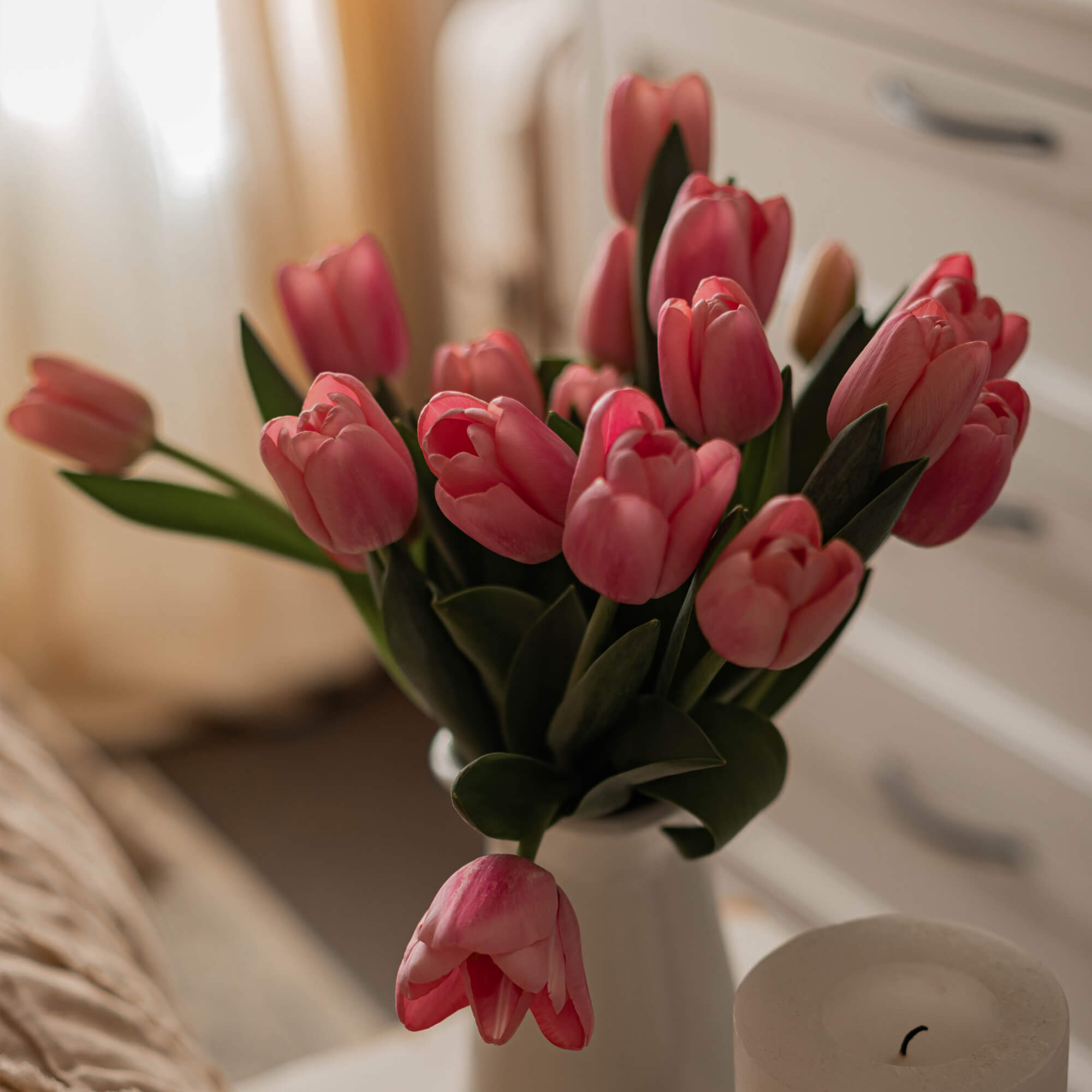 Kytice růžových tulipánů v bílém váze na pozadí světlé ložnice
