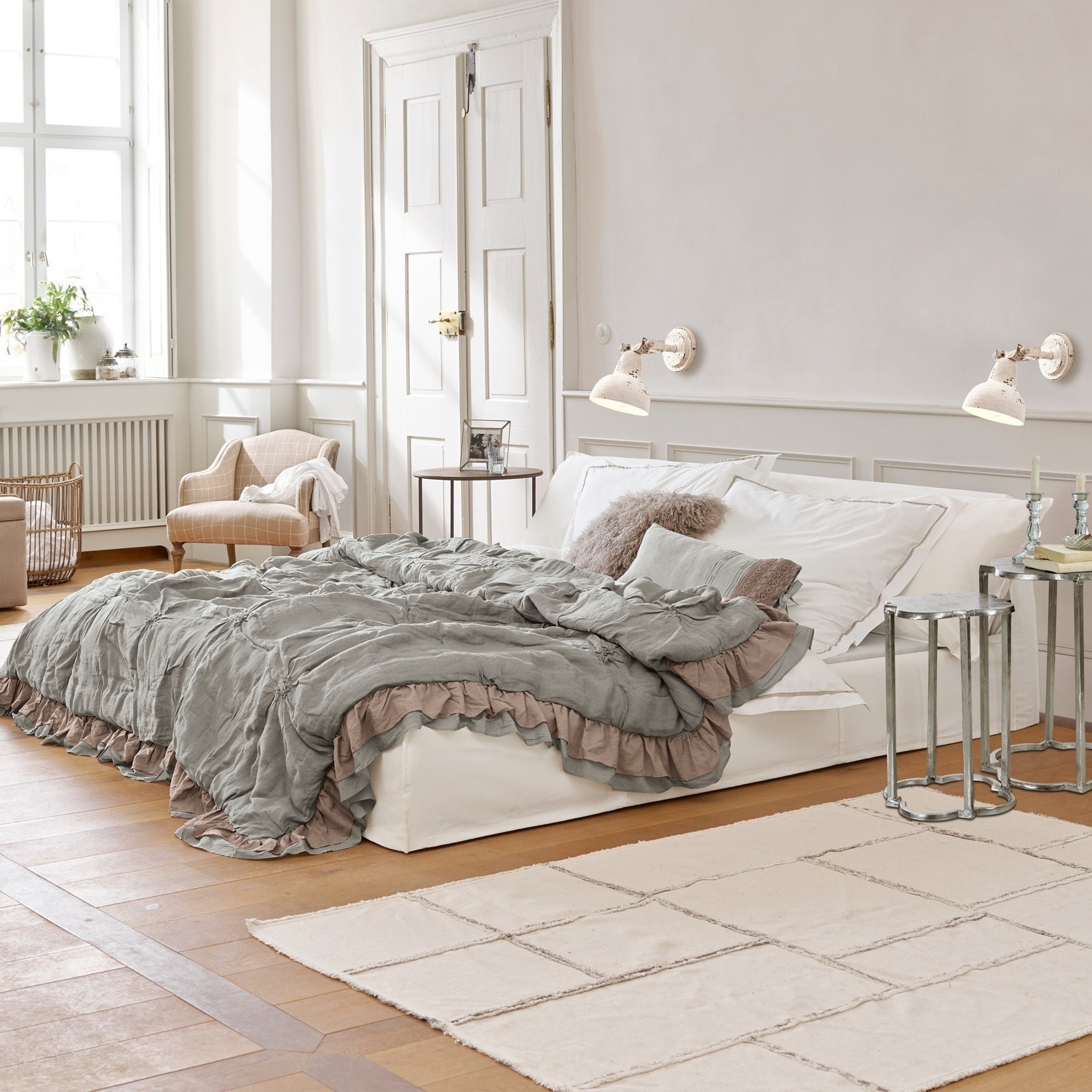Postel Cottonwood Pohodlná ložnice s bílou postelí a šedozelenou přikrývkou s volánky na dřevěné podlaze