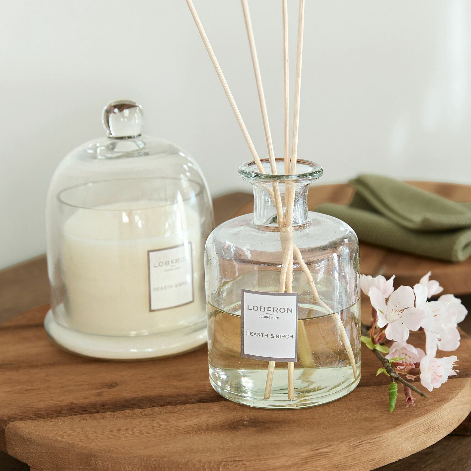Vonná sada Vanis Skleněný aroma difuzér Hearth & Birch s tyčinkami na dřevěném stole, bílá svíčka pod skleněným poklopem