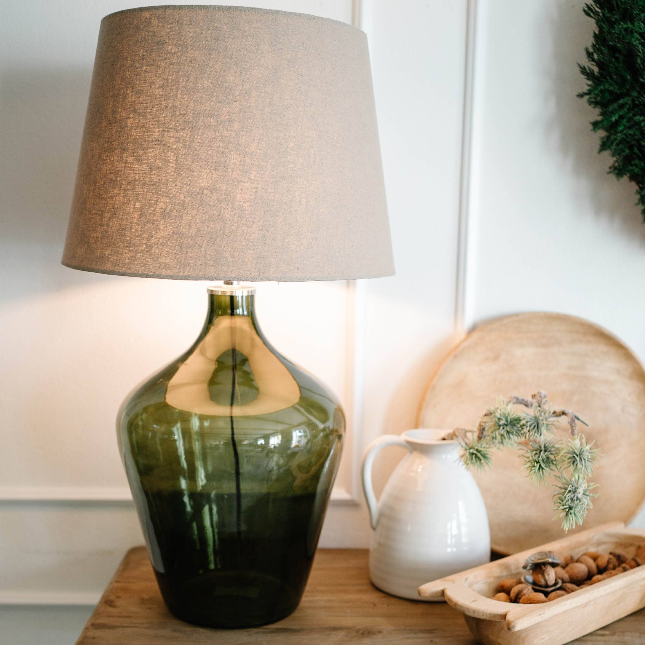 Stolní lampa ze zeleného skla s béžovým stínidlem na dřevěném stole s dekoracemi