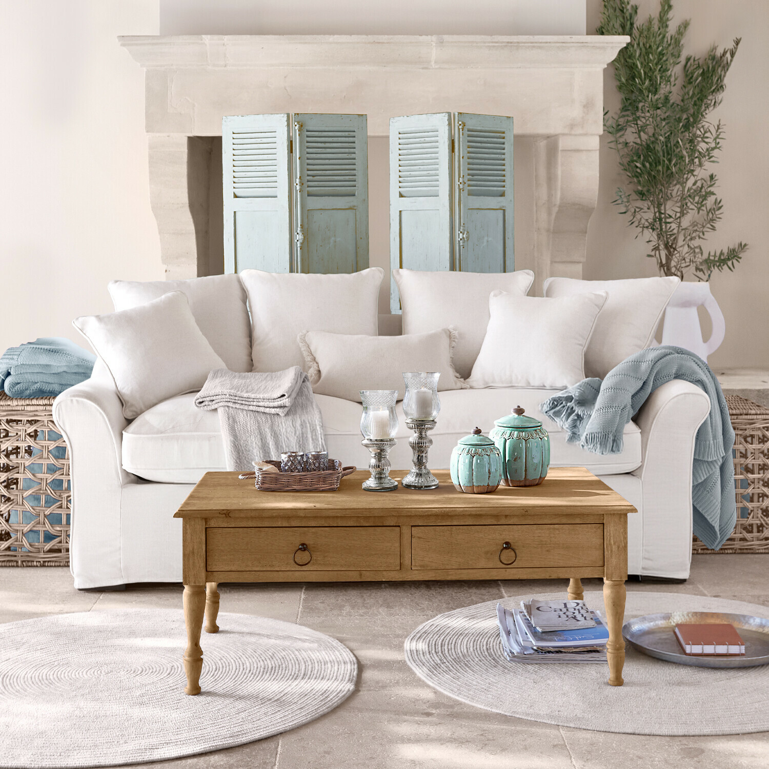 Béžová pohovka s polštáři a dřevěný konferenční stolek s dekoracemi v světlém obývacím pokoji s krbem