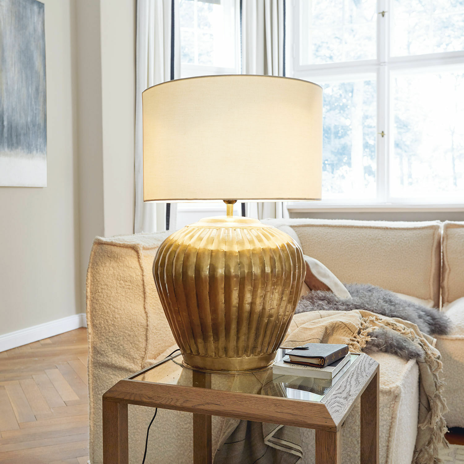 Stolní lampa Fauville Zlatá kovová stolní lampa s béžovým stínidlem na skleněném stolku v světlém obývacím pokoji