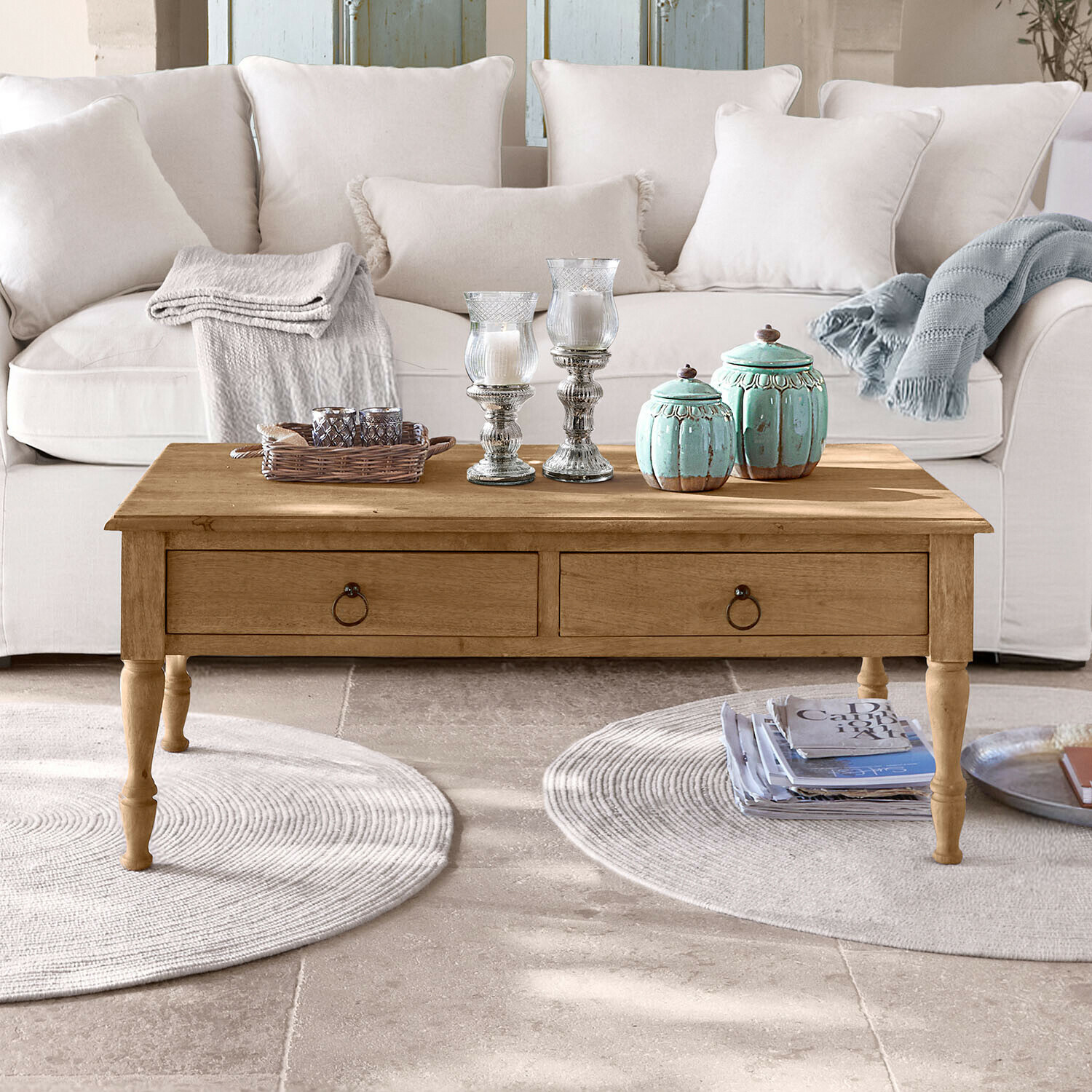 Dřevěný konferenční stolek s šuplíky před světlou pohovkou, dekorace a deky na desce