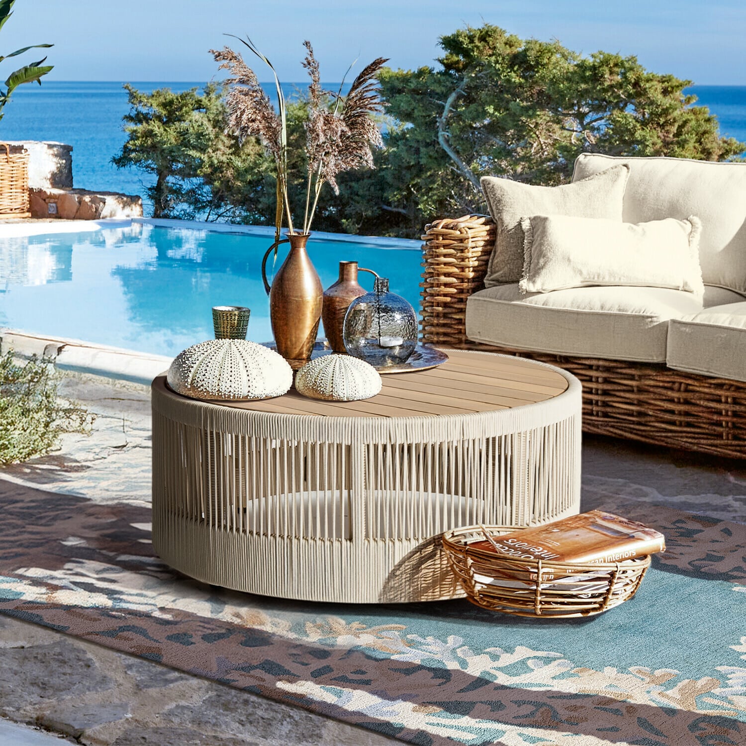 Konferenční stolek Delor Kulatý konferenční stolek z béžového lana a dřeva na terase u bazénu s dekoracemi a proutěnou pohovkou