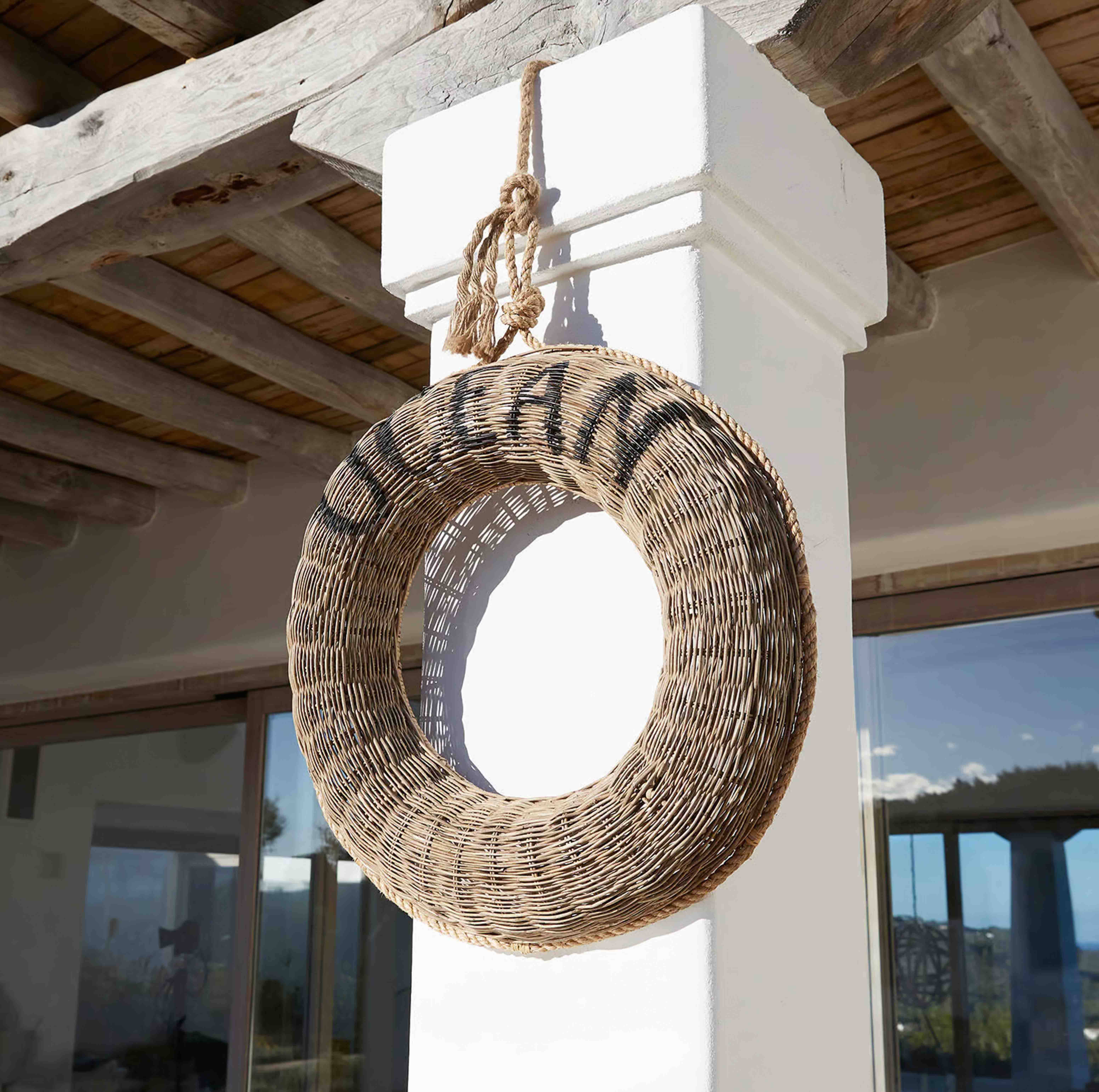 Kulovitý věnec z přírodního proutí zavěšený na bílé sloupu pod dřevěným stropem