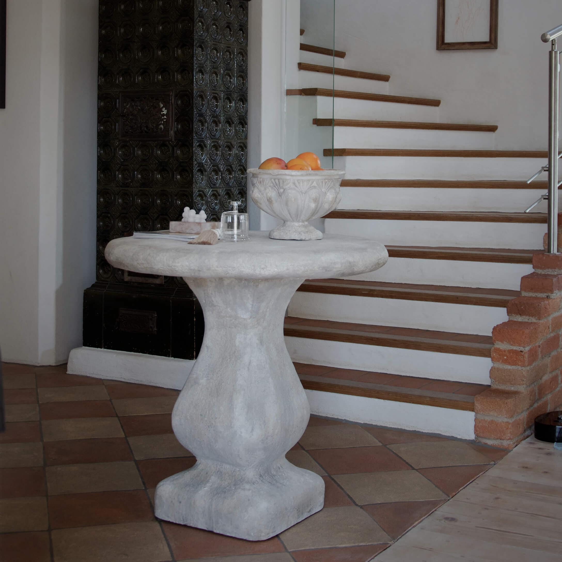 Kulatý šedý betonový stůl u schodiště, dekorativní mísa s ovocem na desce