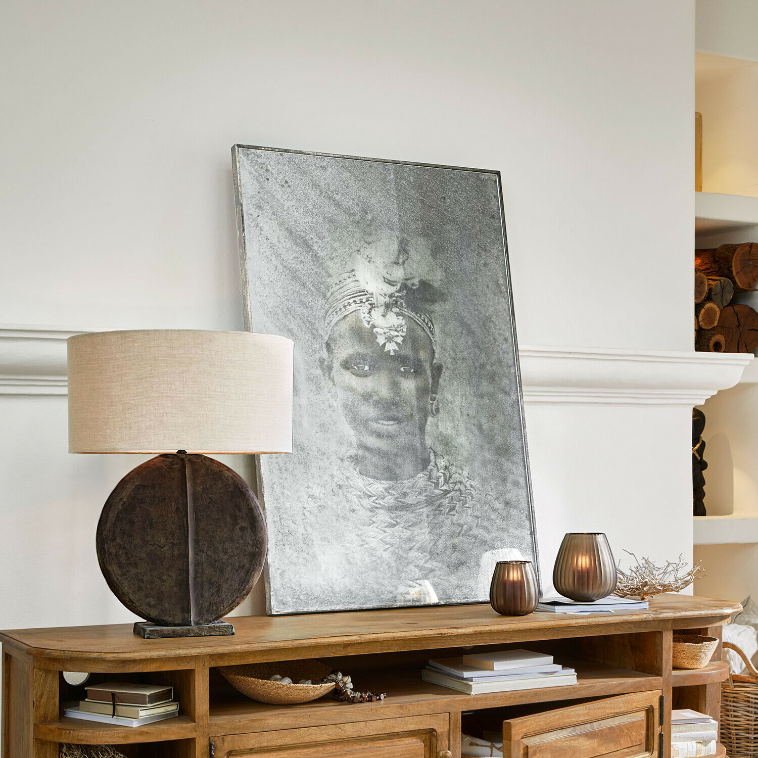 Dekorativní lampa s kulatou základnou a stínidlem na dřevěné komodě s obrazem a svíčkami