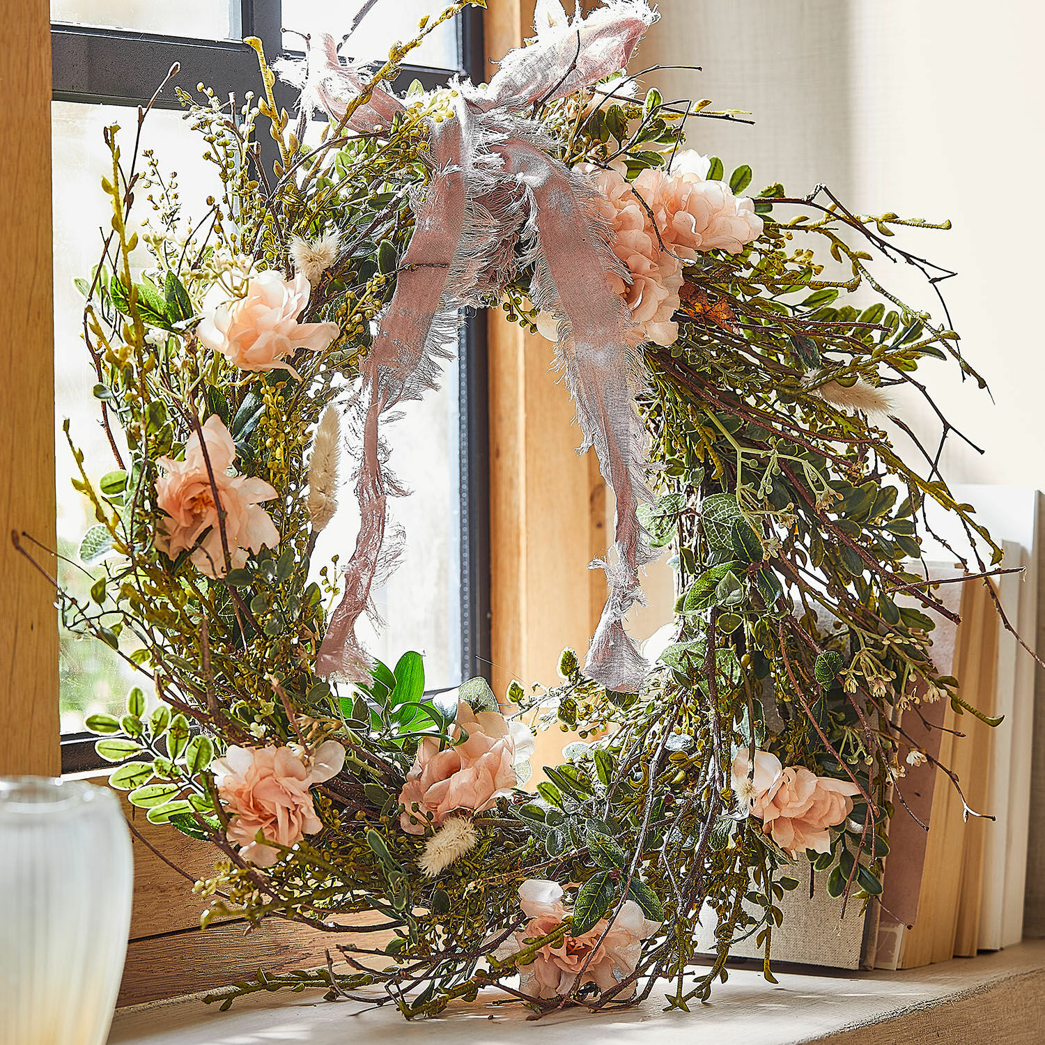 Věnec Chérisse Dekorativní věnec z větviček, růžových květů a zelených listů s růžovou stuhou na okně