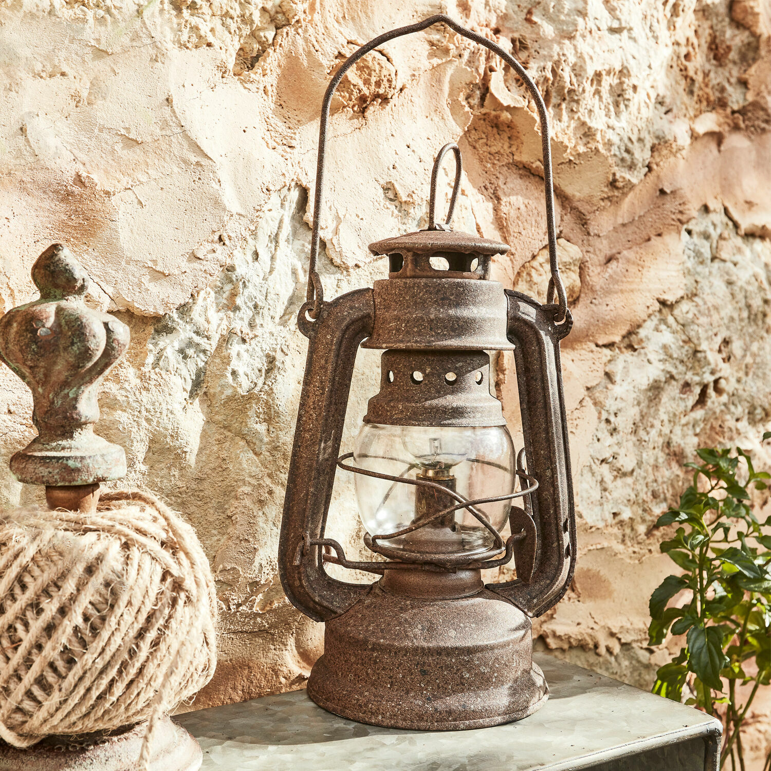 Rustikální kovová petrolejová lampa s rezavým povrchem na pozadí kamenné zdi, vintage dekorace