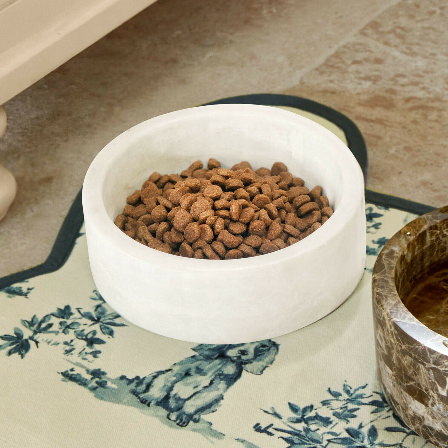 Bílá mramorová miska na krmivo s hnědým krmivem na dekorativní podložce s motivem psa