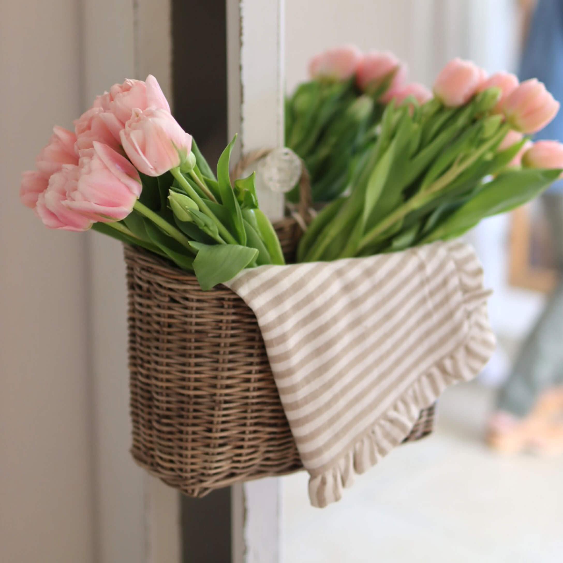 Proutěný koš s růžovými tulipány a bavlněnou pruhovanou utěrkou pro domácí dekoraci