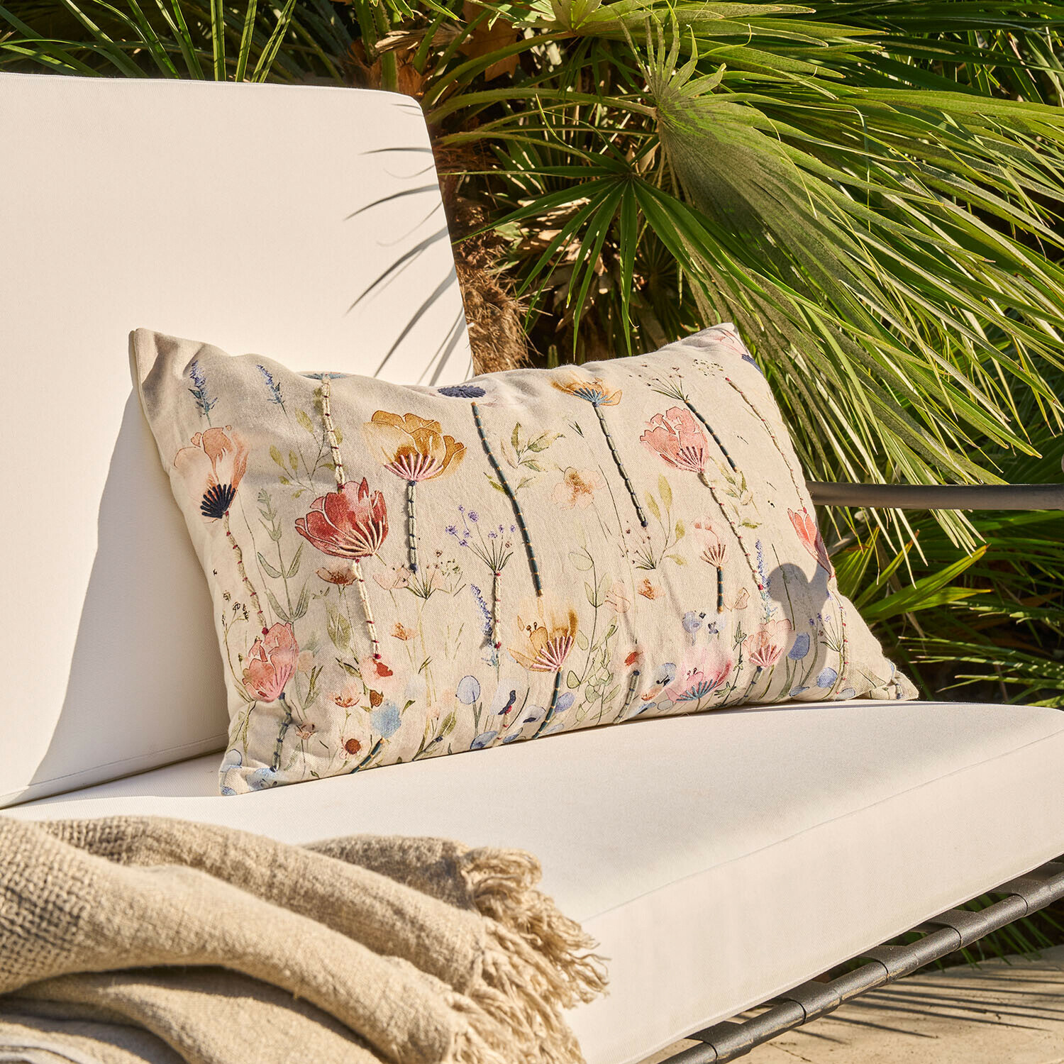 Béžový dekorativní polštář s květinovým vzorem na světlém zahradním křesle s dekou