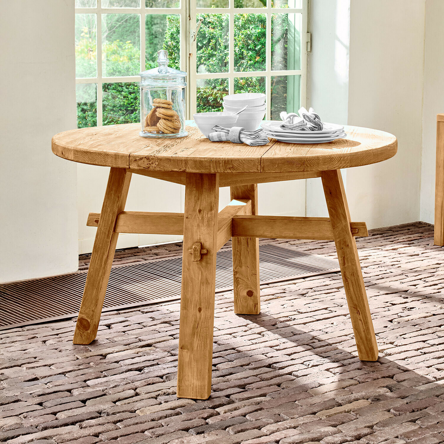 Stůl Crestwooden Kulatý stůl z přírodního borovicového dřeva na cihlové podlaze u okna
