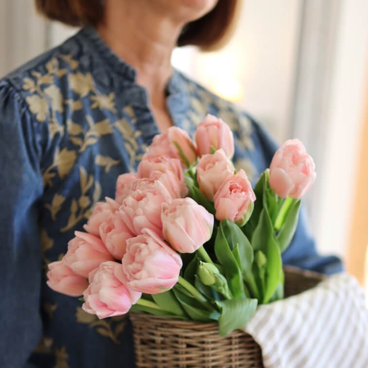 Kytice růžových tulipánů v proutěném koši drženém ženou v modré květované blůze