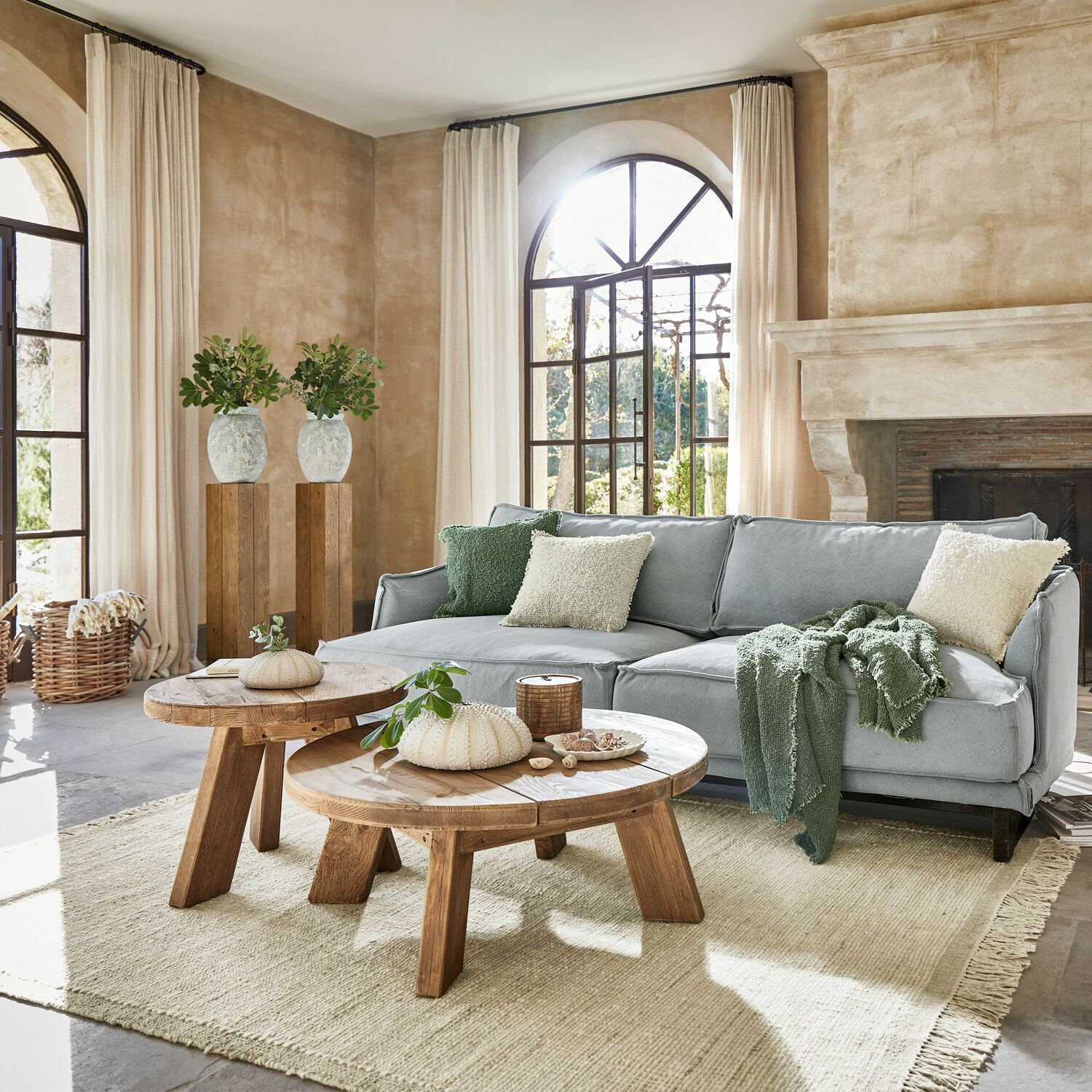 Pohodlný obývací pokoj se šedou pohovkou, dřevěnými stolky a světlým přírodním kobercem