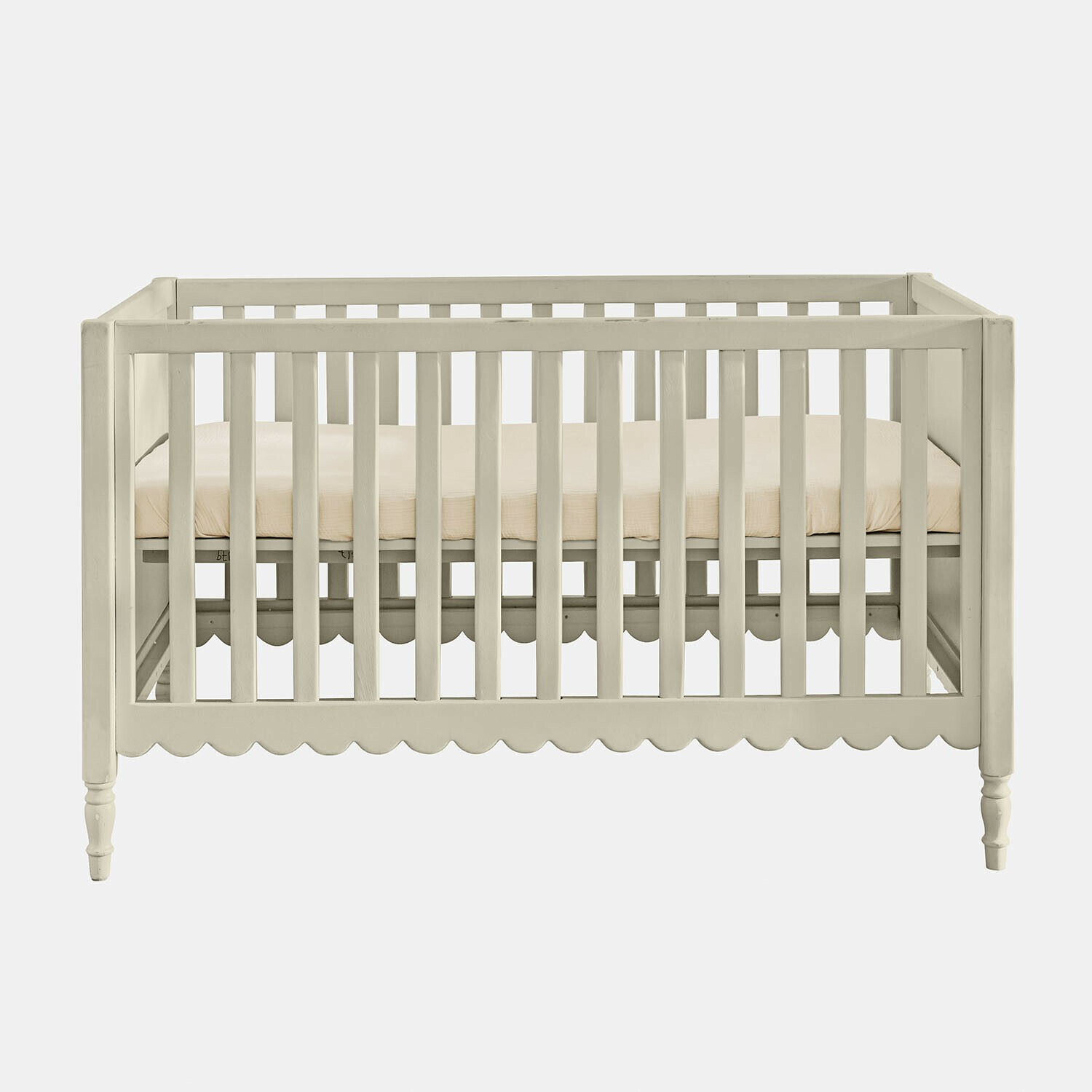 Bílé dětské dřevěné postýlka s béžovou matrací a ozdobným vlnkovaným okrajem dole