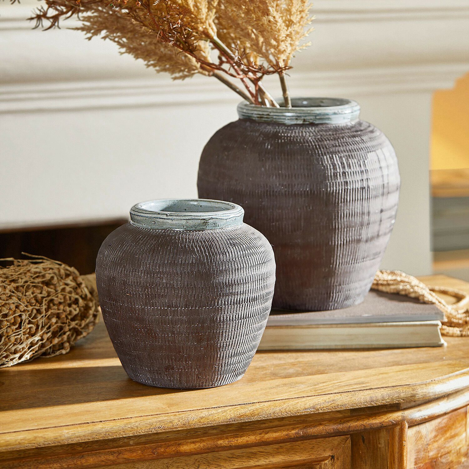 Dvě dekorativní hnědé keramické vázy na dřevěném stole se sušenými rostlinami