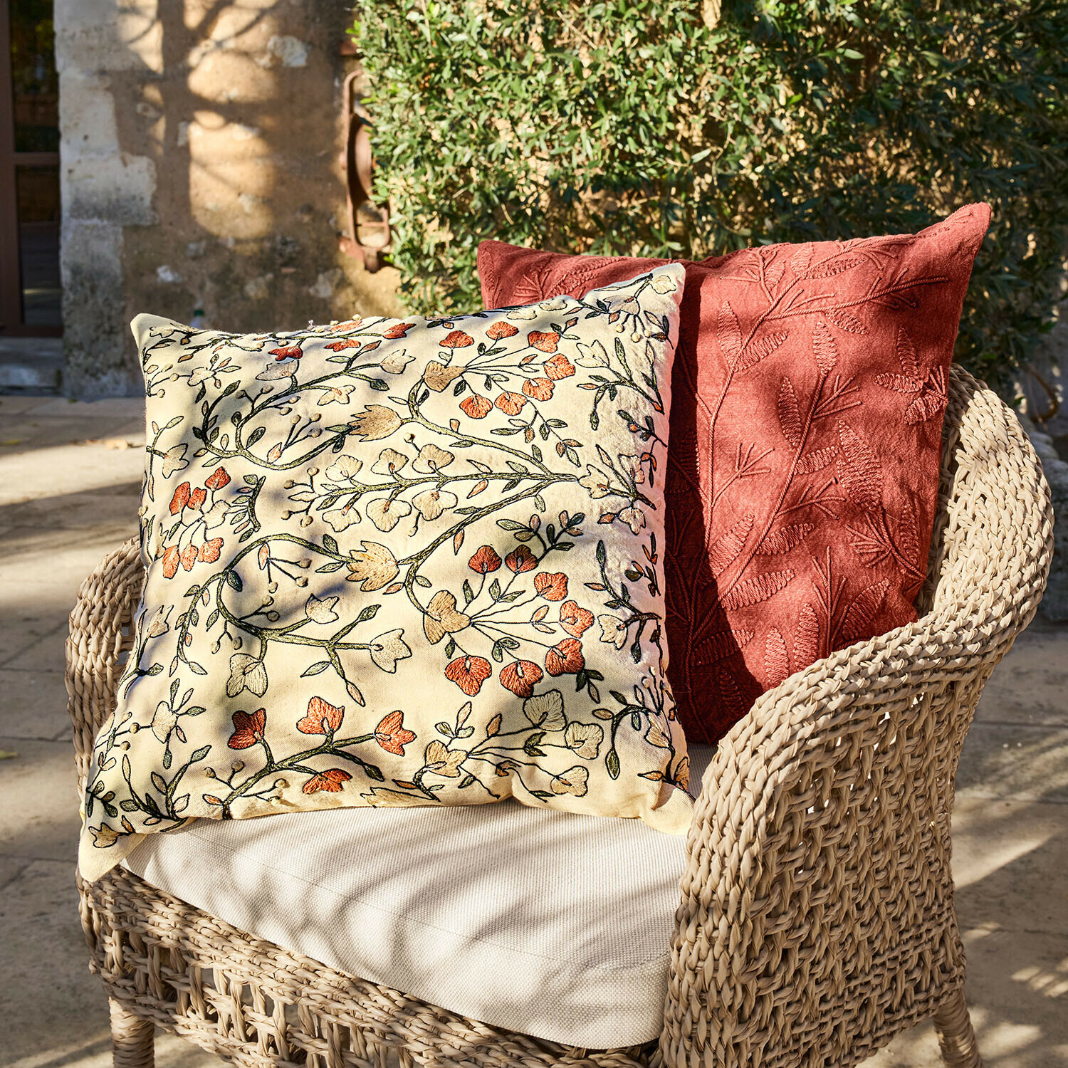 Dva dekorativní polštáře s květinovou a listovou výšivkou na proutěném křesle venku