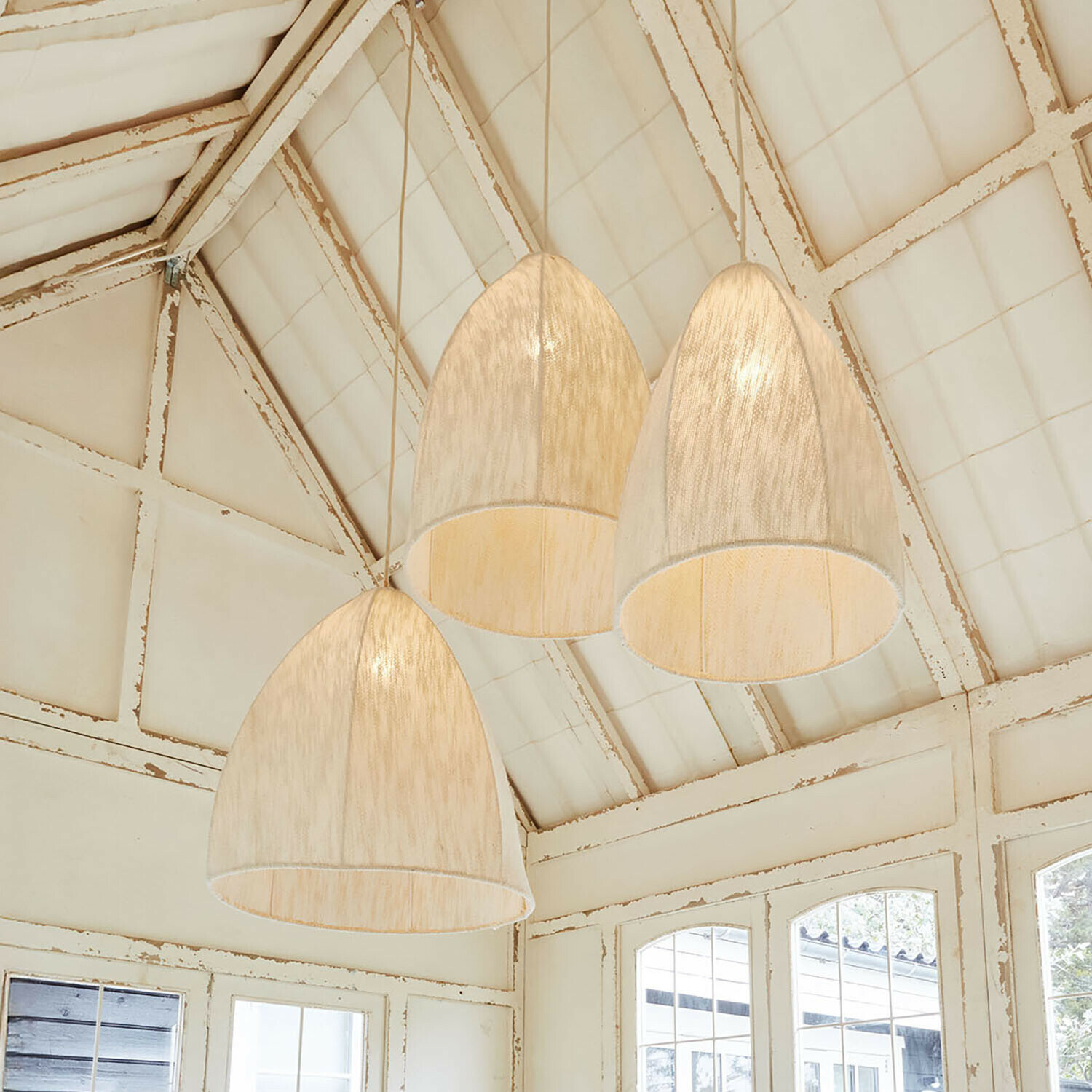 Tři závěsná světla z světlého materiálu ve tvaru zvonu v rustikálním interiéru s bílým stropem