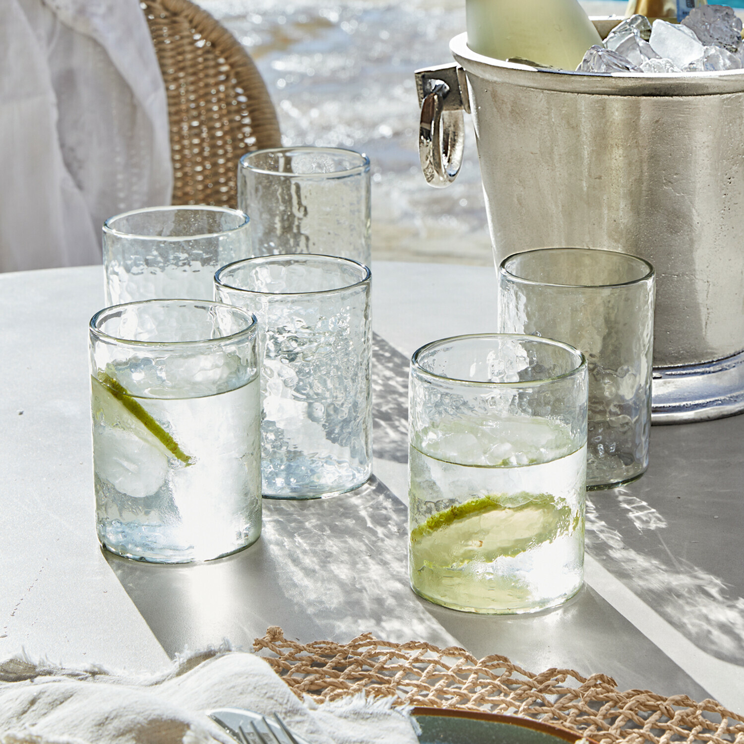 Sklenice z průhledného texturovaného skla s plátky limetky a ledem na bílém stole