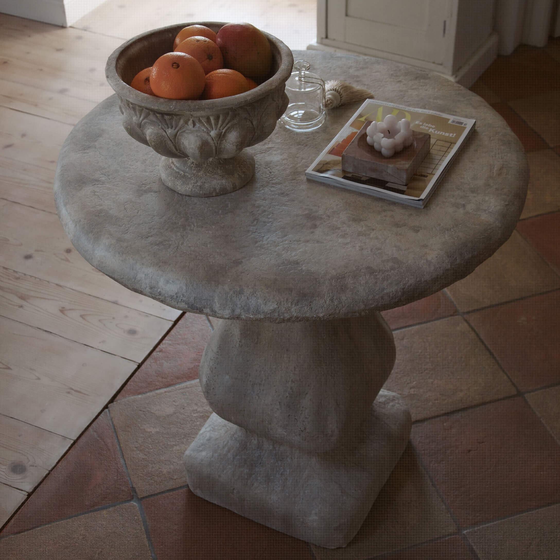 Kulatý šedý kamenný stůl s miskou na ovoce a dekorativními předměty na desce