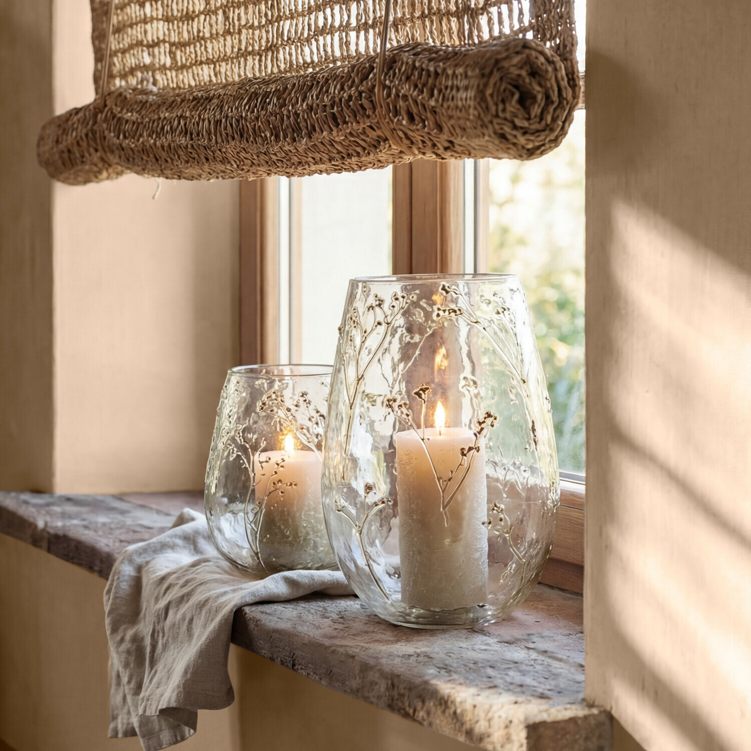 Nádobky na svíčku, 2dílná sada Elorisse Skleněné svícny s rostlinným reliéfem a bílými svíčkami na kamenném parapetu za denního světla